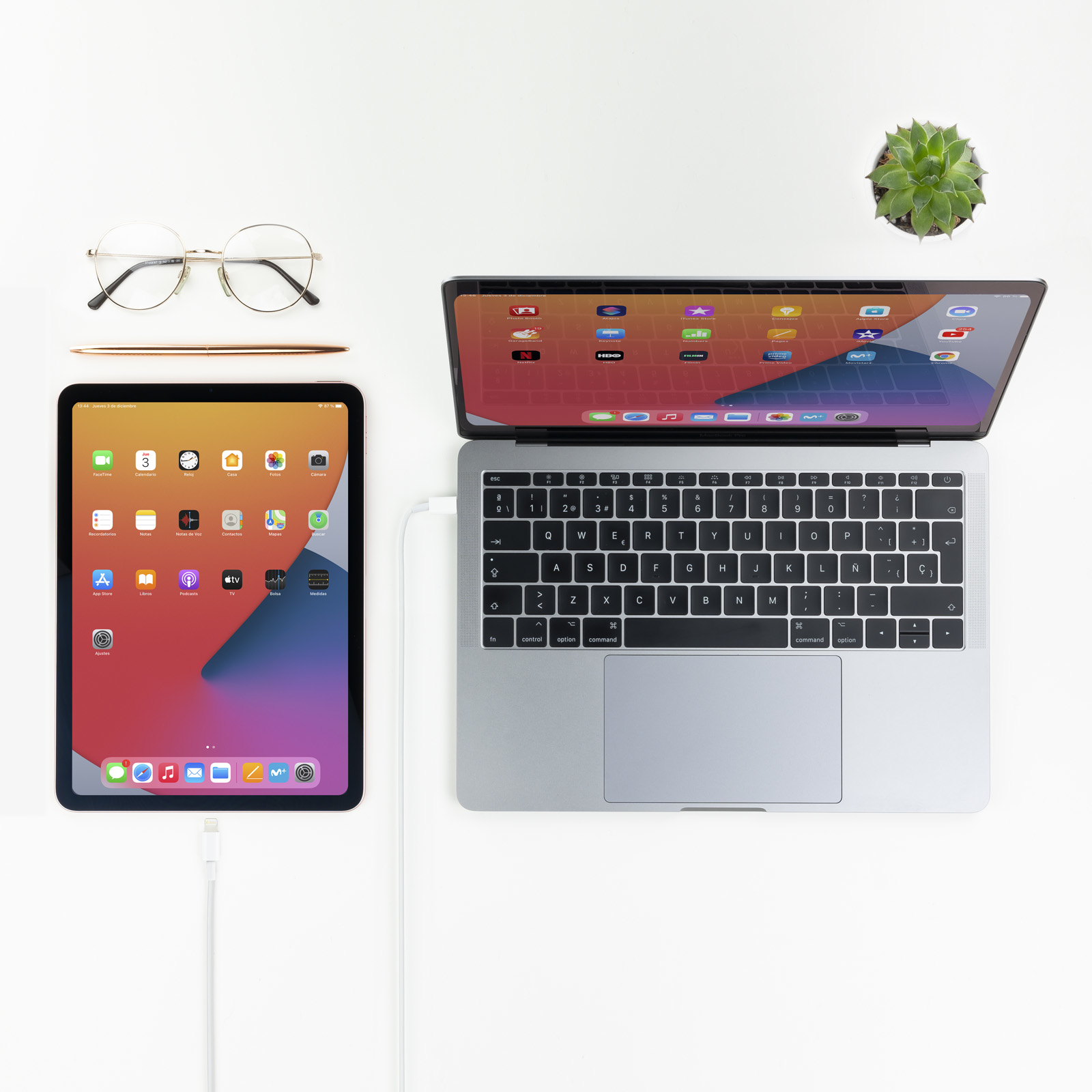 Vista superior de un iPad, un portátil y accesorios sobre una superficie blanca.