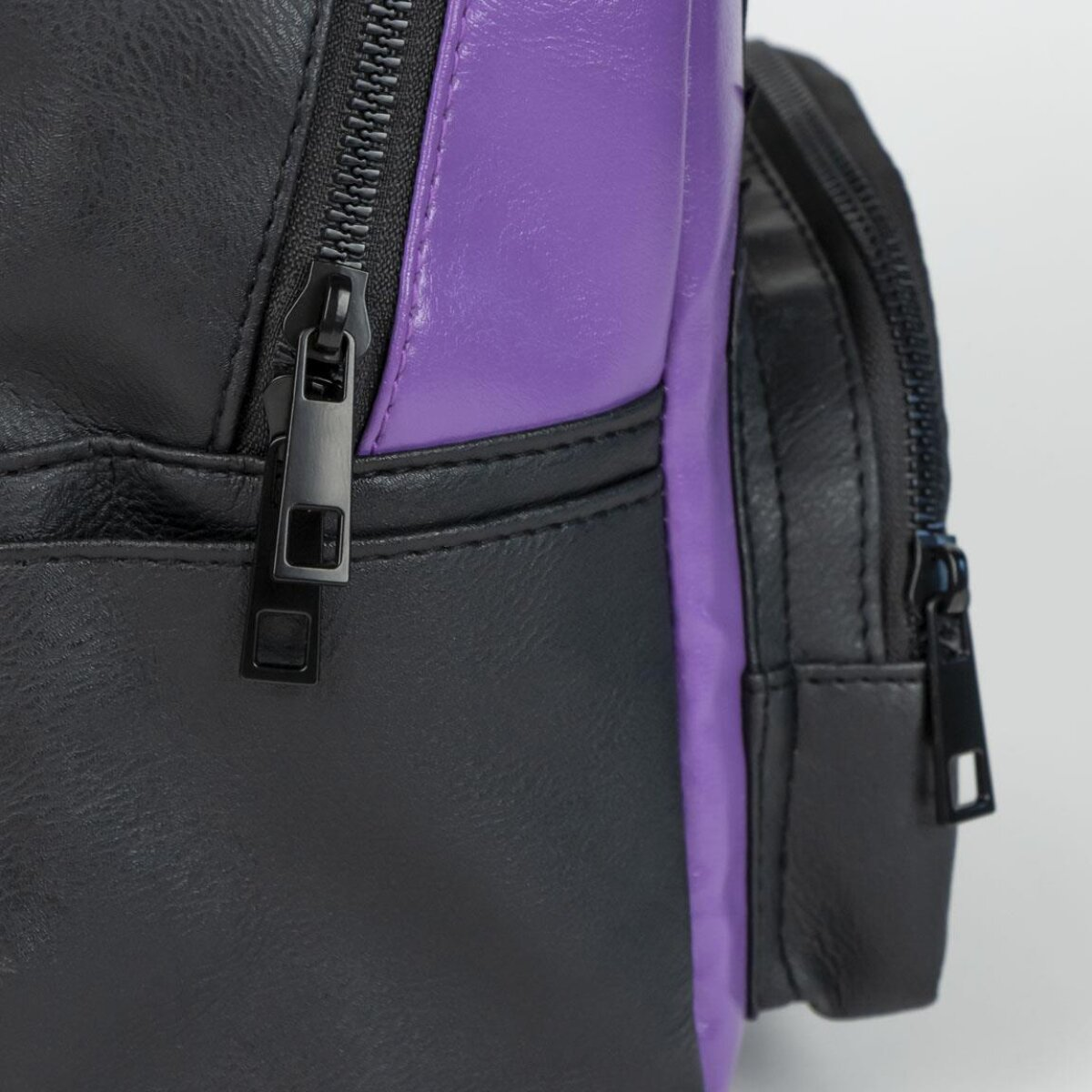 Primer plano de mochila negra y morada con cremallera y tirador negro.