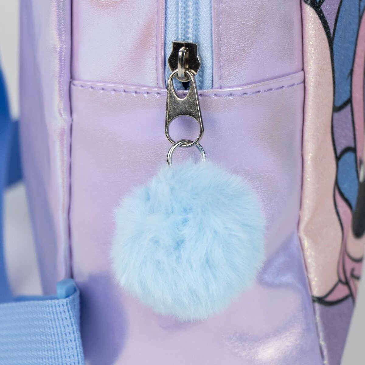 Primer plano de un pompón azul adjunto a la cremallera de una mochila morada.