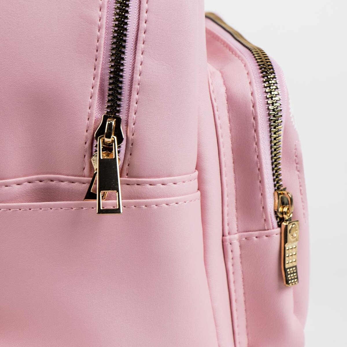 Mochila rosa con cremalleras doradas y fondo blanco. Se ven las cremalleras.