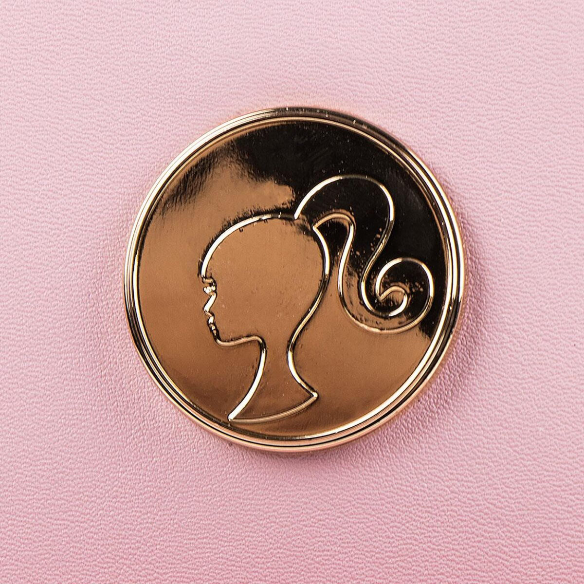 Logotipo dorado de Barbie en la superficie de una bolsa rosa. Silueta en un círculo.