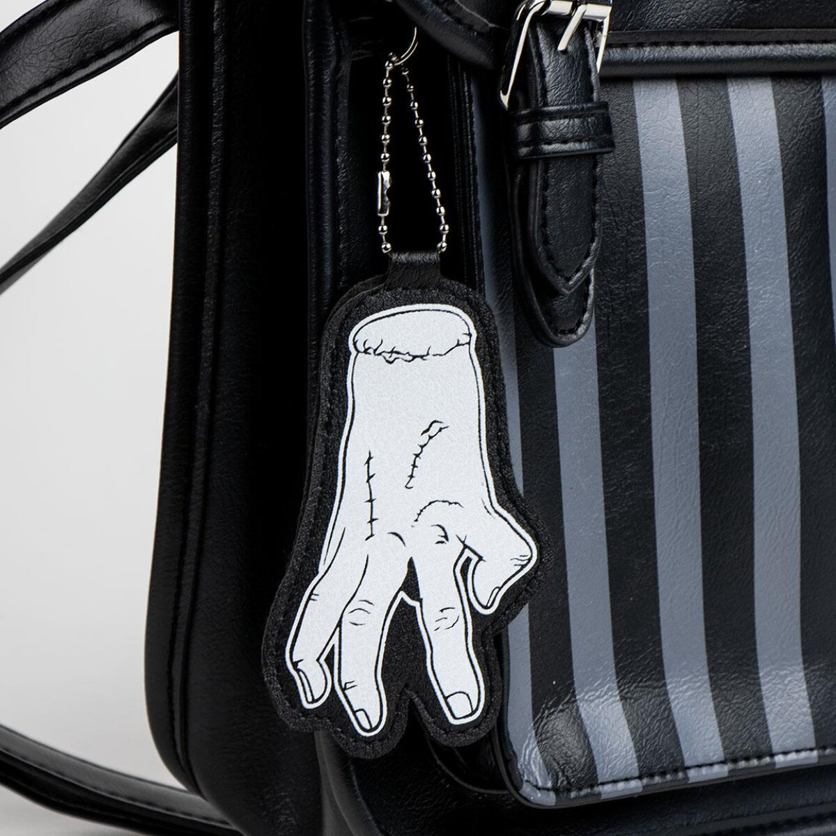Schwarze Tasche mit handförmigem Anhänger. Die Tasche hat ein Streifenmuster und eine Schnalle.