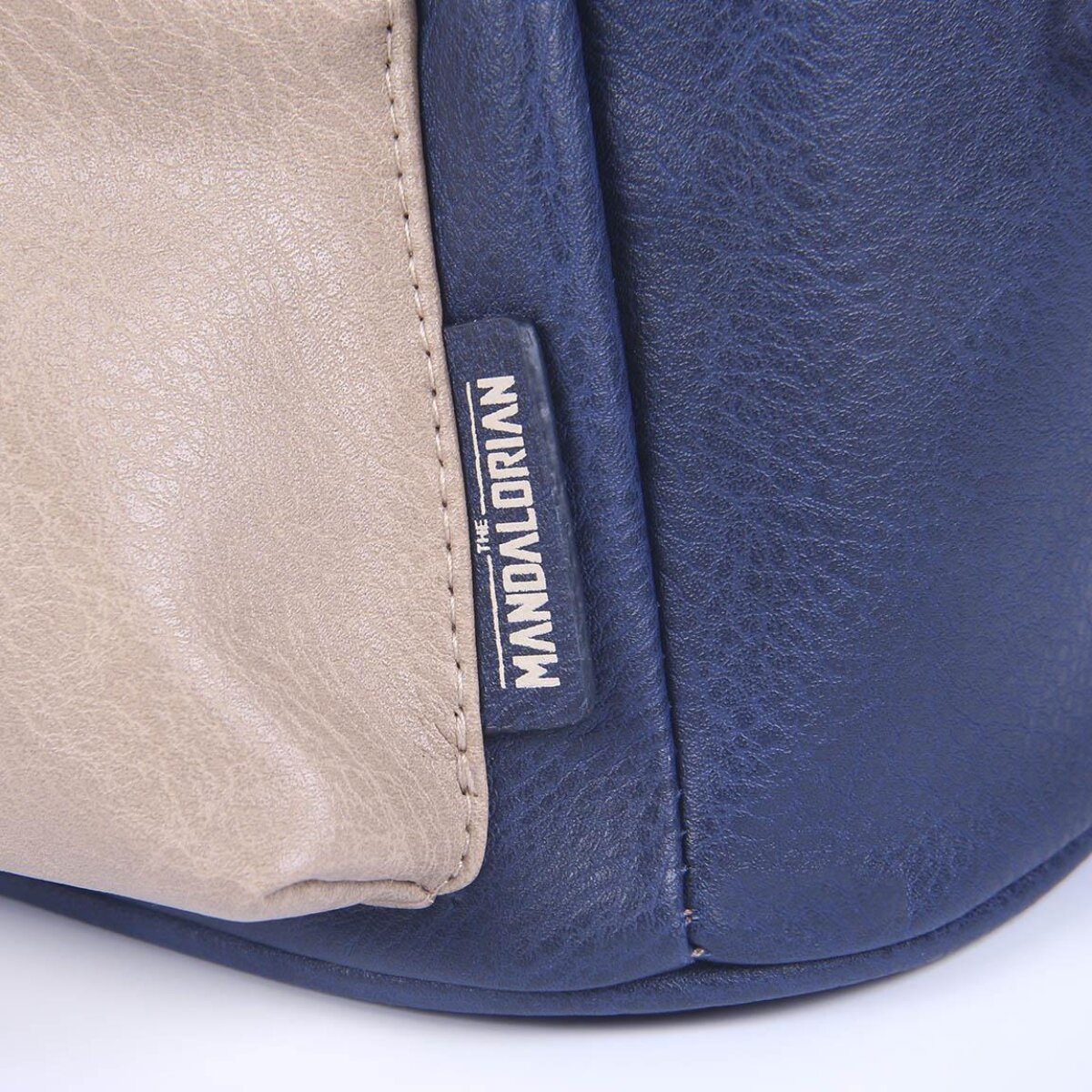 Ein blauer und beigefarbener Rucksack mit einem Etikett mit der Aufschrift 'THE MANDALORIAN'. Die Tasche ist aus Leder.
