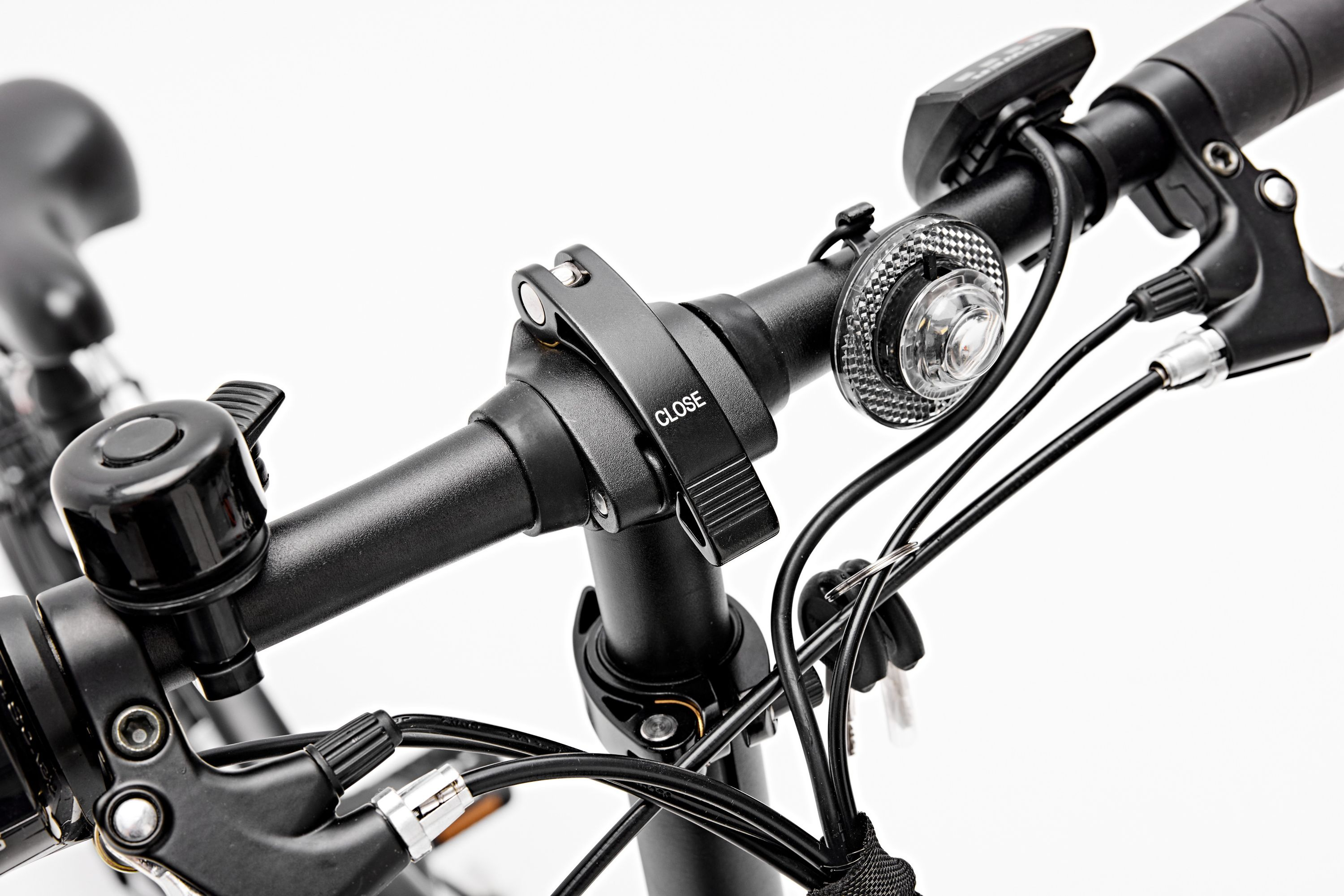 Nahaufnahme des Lenkers eines schwarzen Fahrrads, mit Klingel, Licht und Bedienelementen. Das Wort CLOSE.