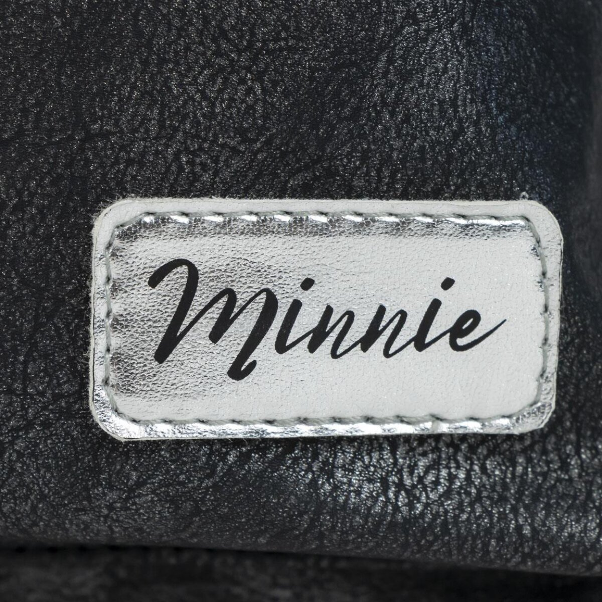 "Minnie" está cosido en cursiva negra en una etiqueta plateada, sobre un fondo negro texturizado.