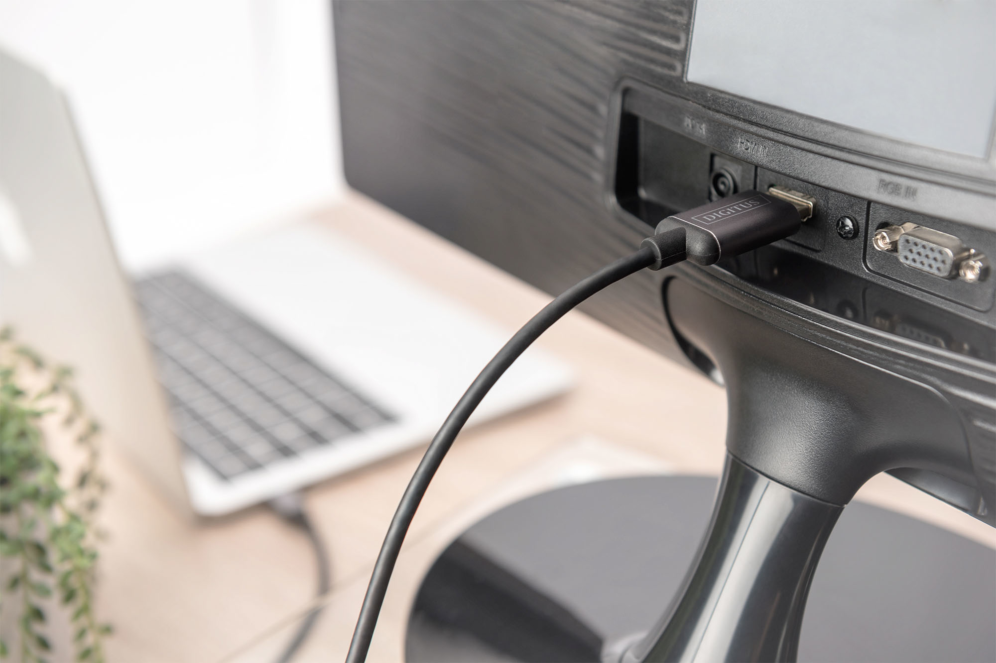 Cable USB-C a HDMI conectado a un monitor, con un portátil en el fondo.
