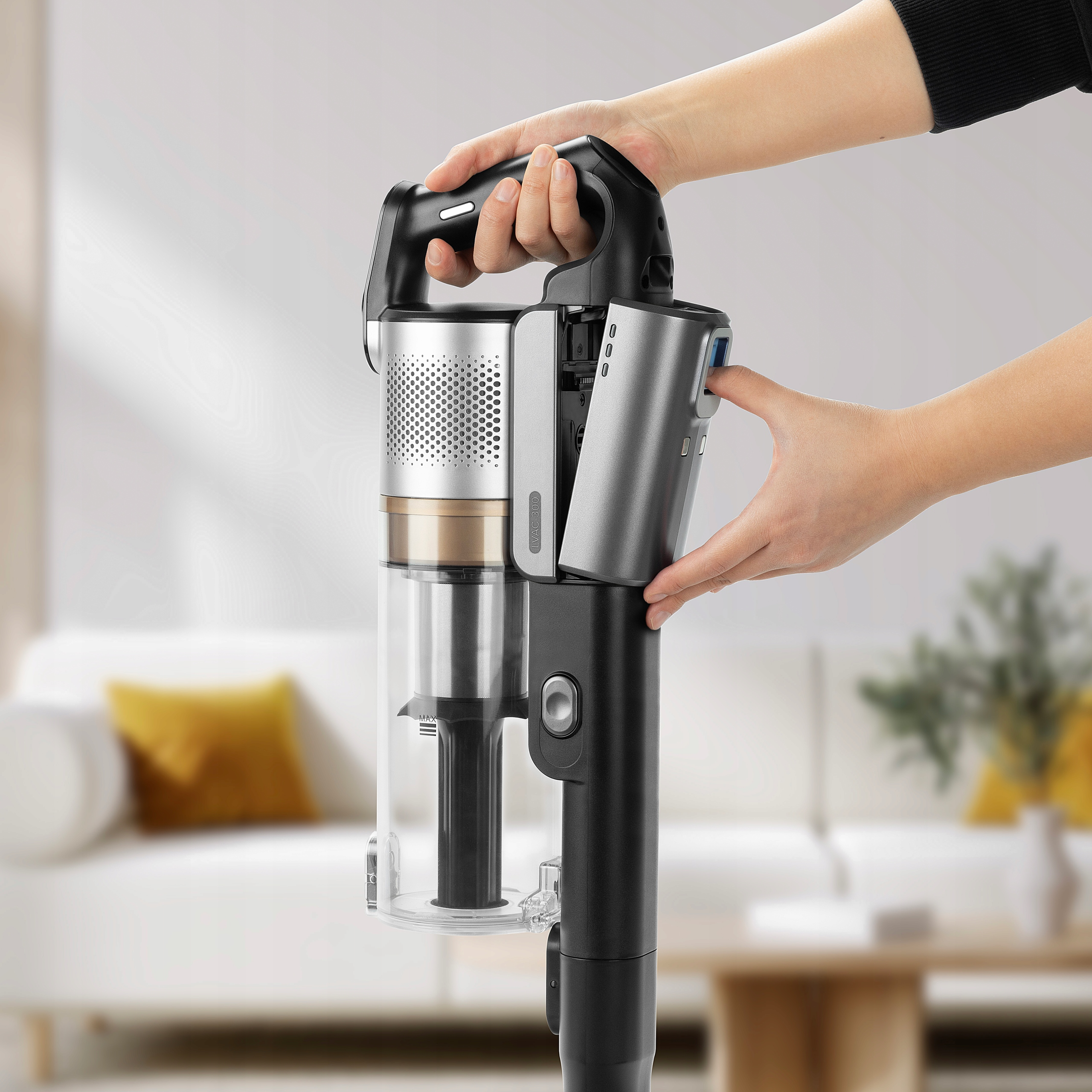 Ręce regulują baterię srebrnego i czarnego bezprzewodowego odkurzacza w jasnym, rozmytym salonie.