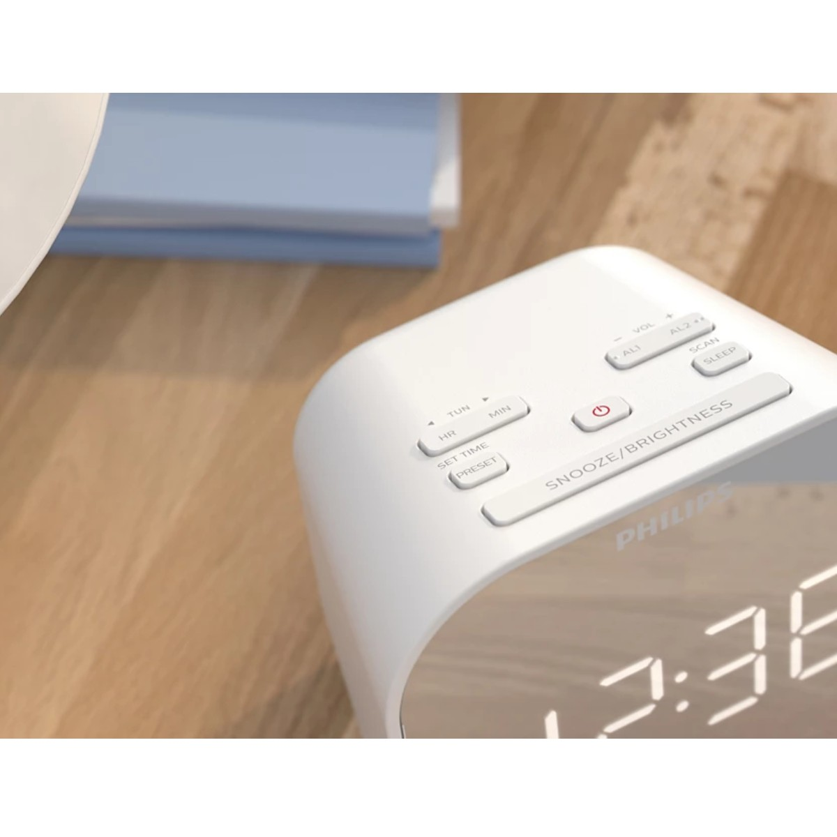 Primer plano de un despertador Philips blanco. Muestra botones para la configuración de la hora y la función de repetición. La pantalla muestra 2:36.