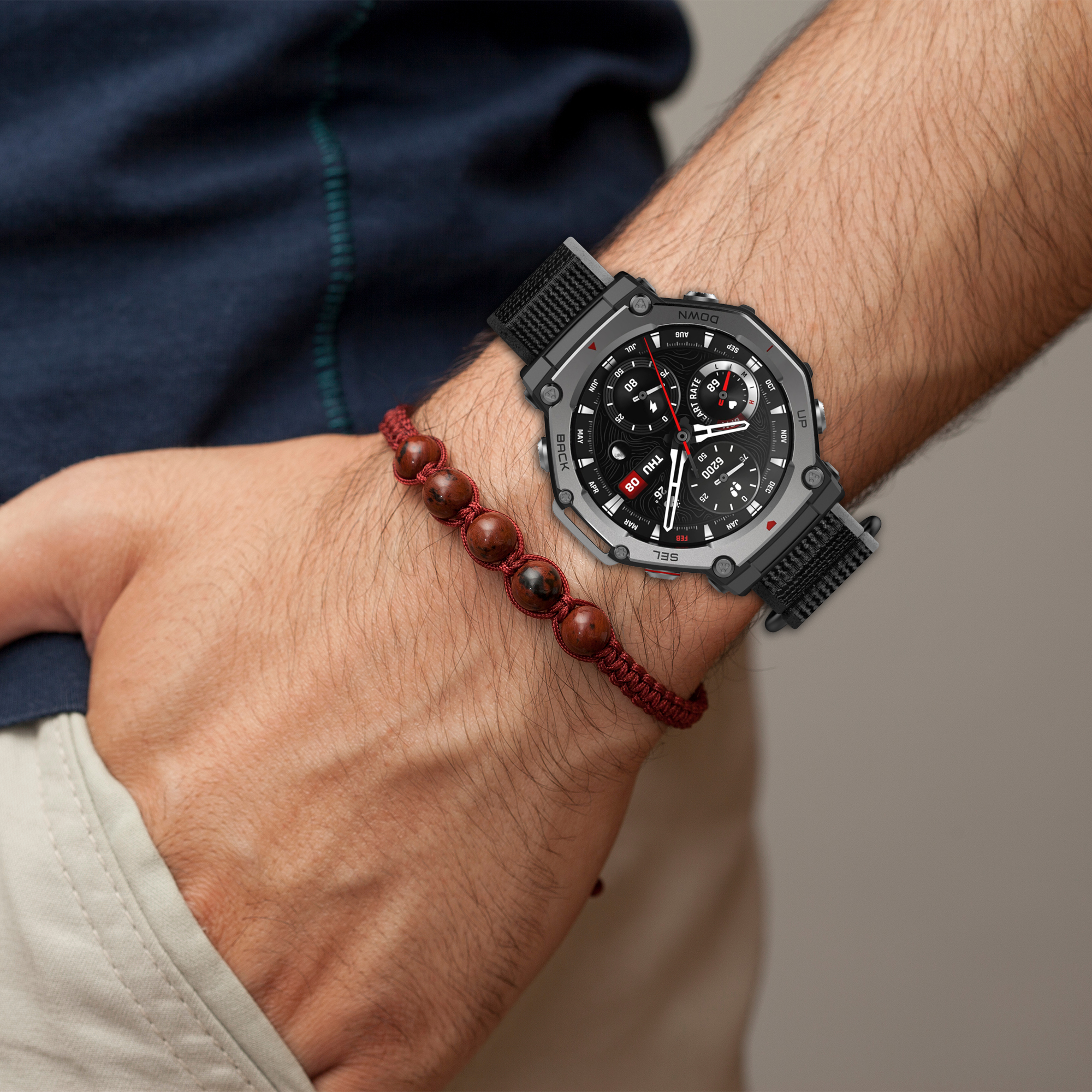 Das Handgelenk eines Mannes mit einer Smartwatch und einem Perlenarmband. Die Uhr hat ein schwarzes Armband und Display.
