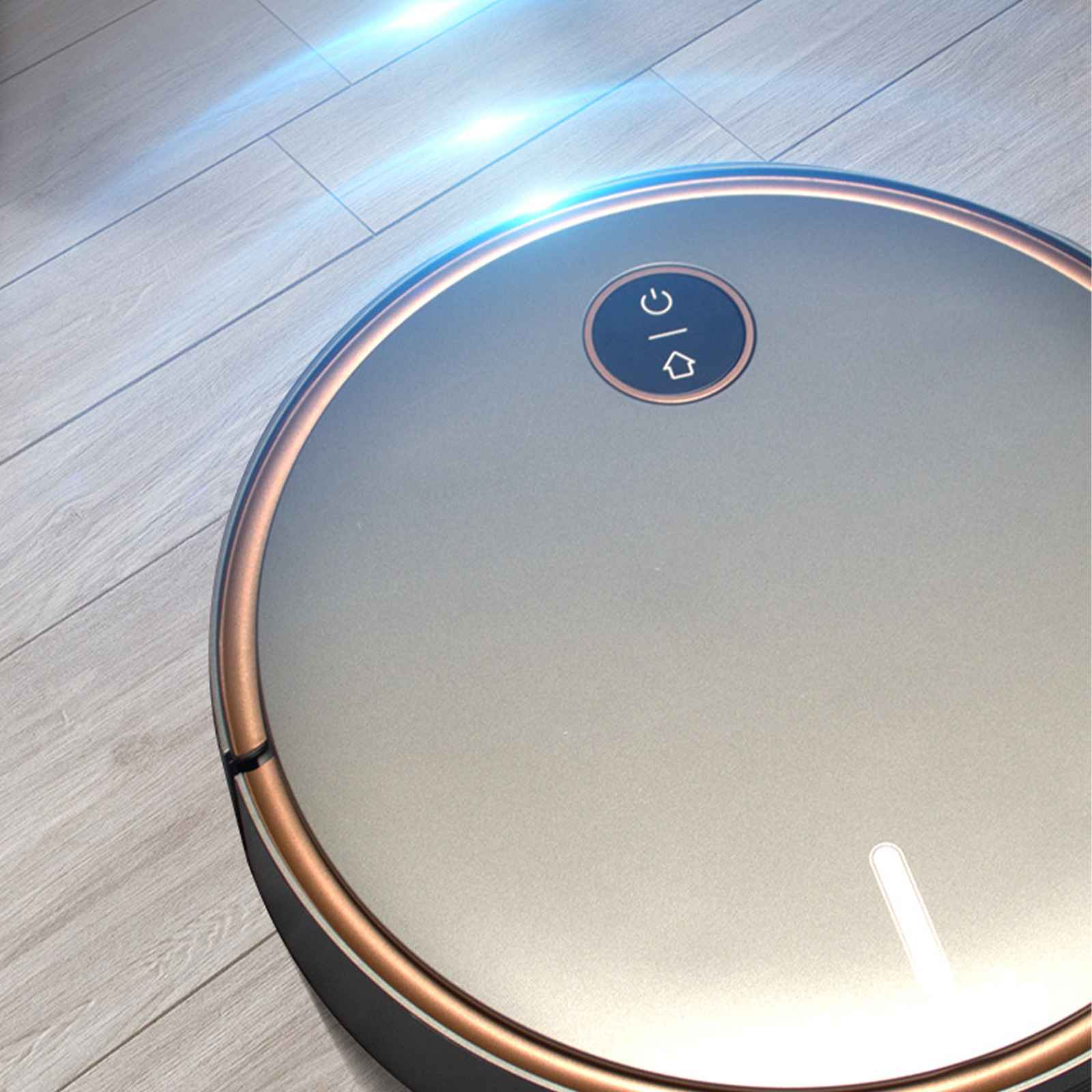 Nahaufnahme eines grauen Roboterstaubsaugers mit Goldrand auf einem Holzboden. Es hat einen Power-Knopf.