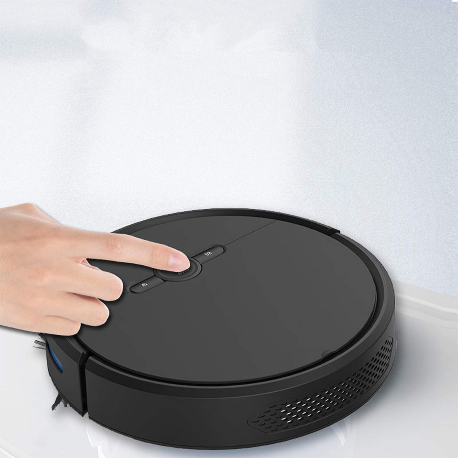 Ein schwarzer Roboter-Staubsauger, der von einer Hand mit einem Knopf in der Mitte eingeschaltet wird.