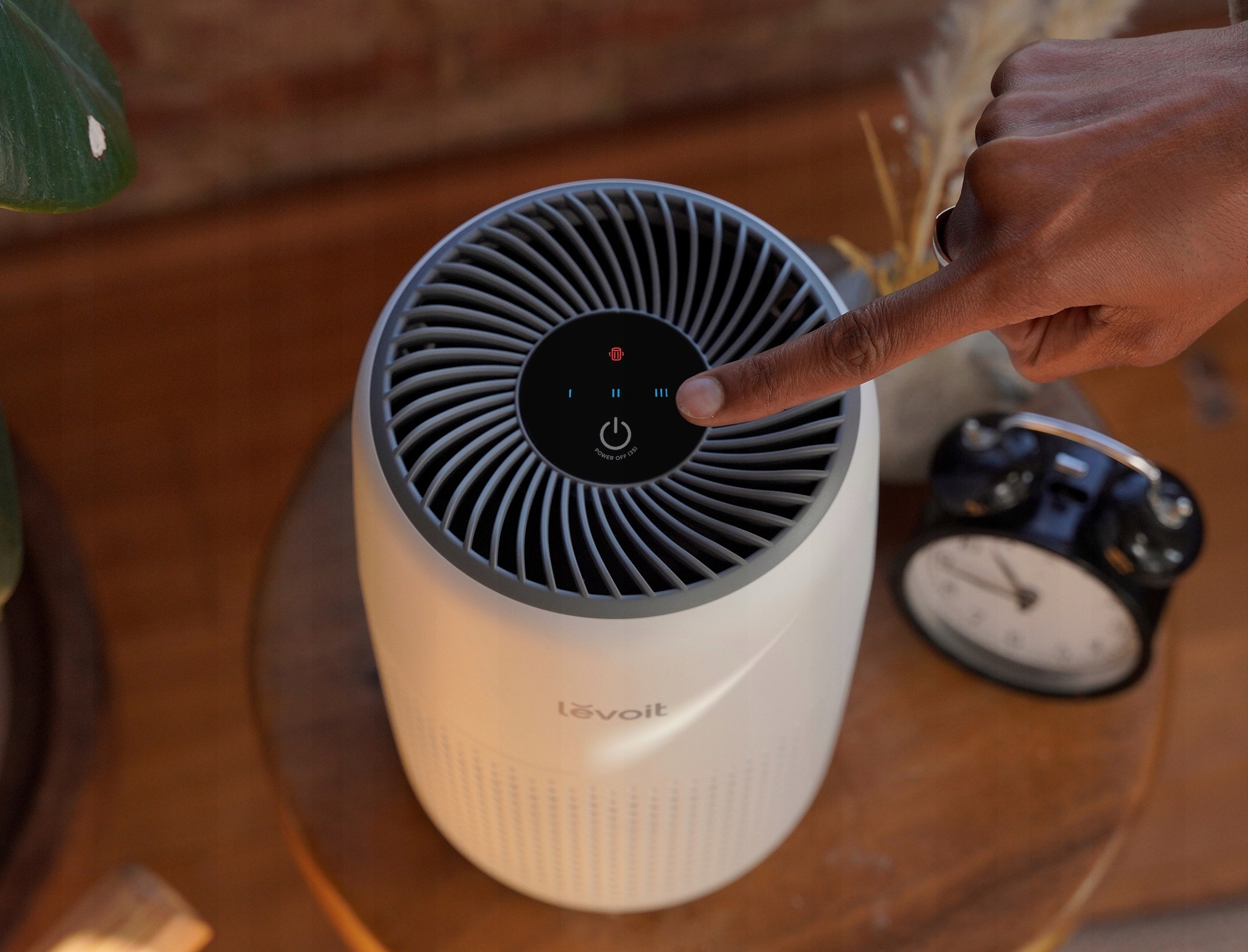 Palec naciska przycisk zasilania na białym i szarym oczyszczaczu powietrza Levoit.