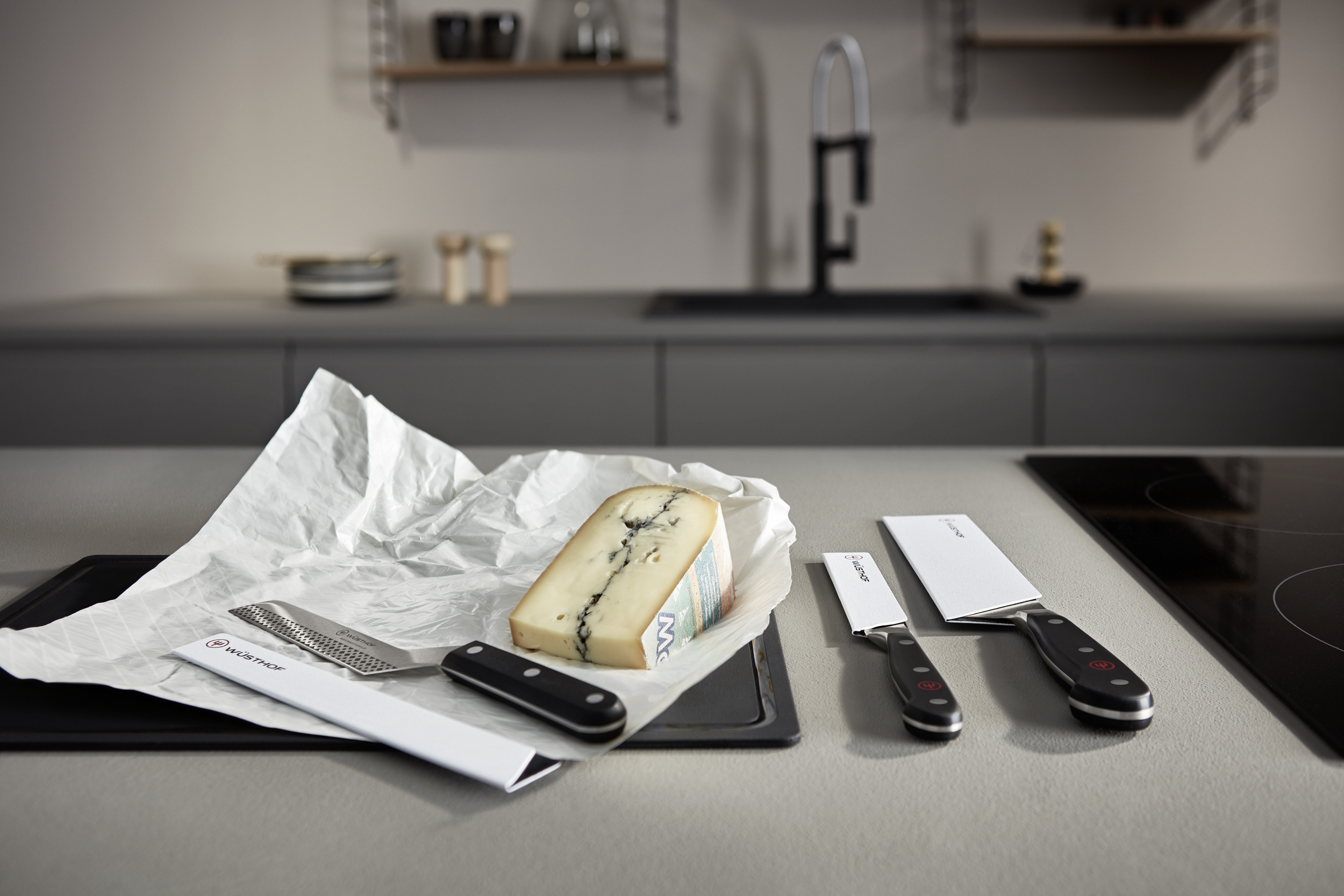 Käse, Messer und ein Reibeisen auf einer Küchenarbeitsplatte. Die Szene ist gut beleuchtet.