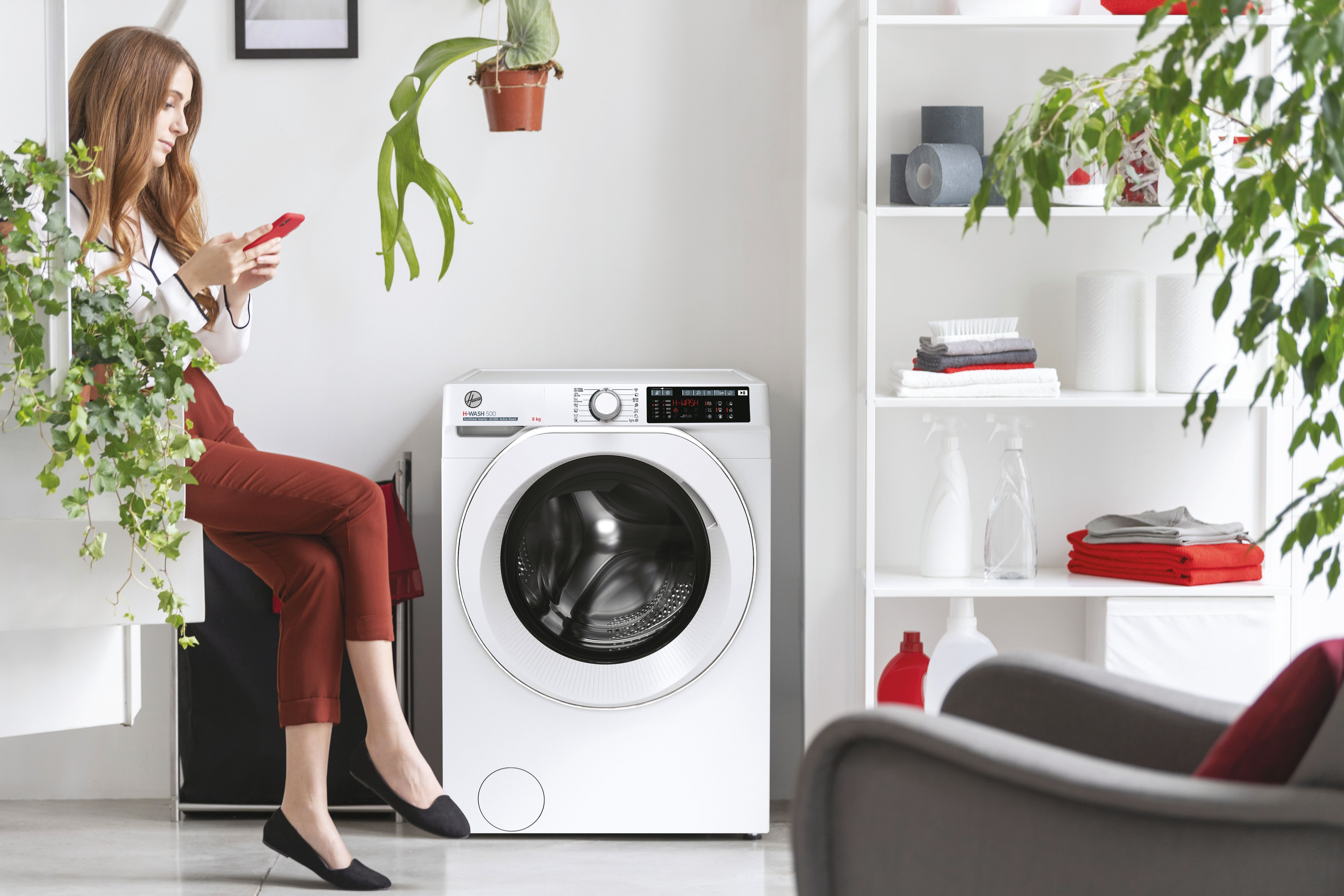 Een vrouw zit in de buurt van een witte wasmachine terwijl ze haar telefoon gebruikt.