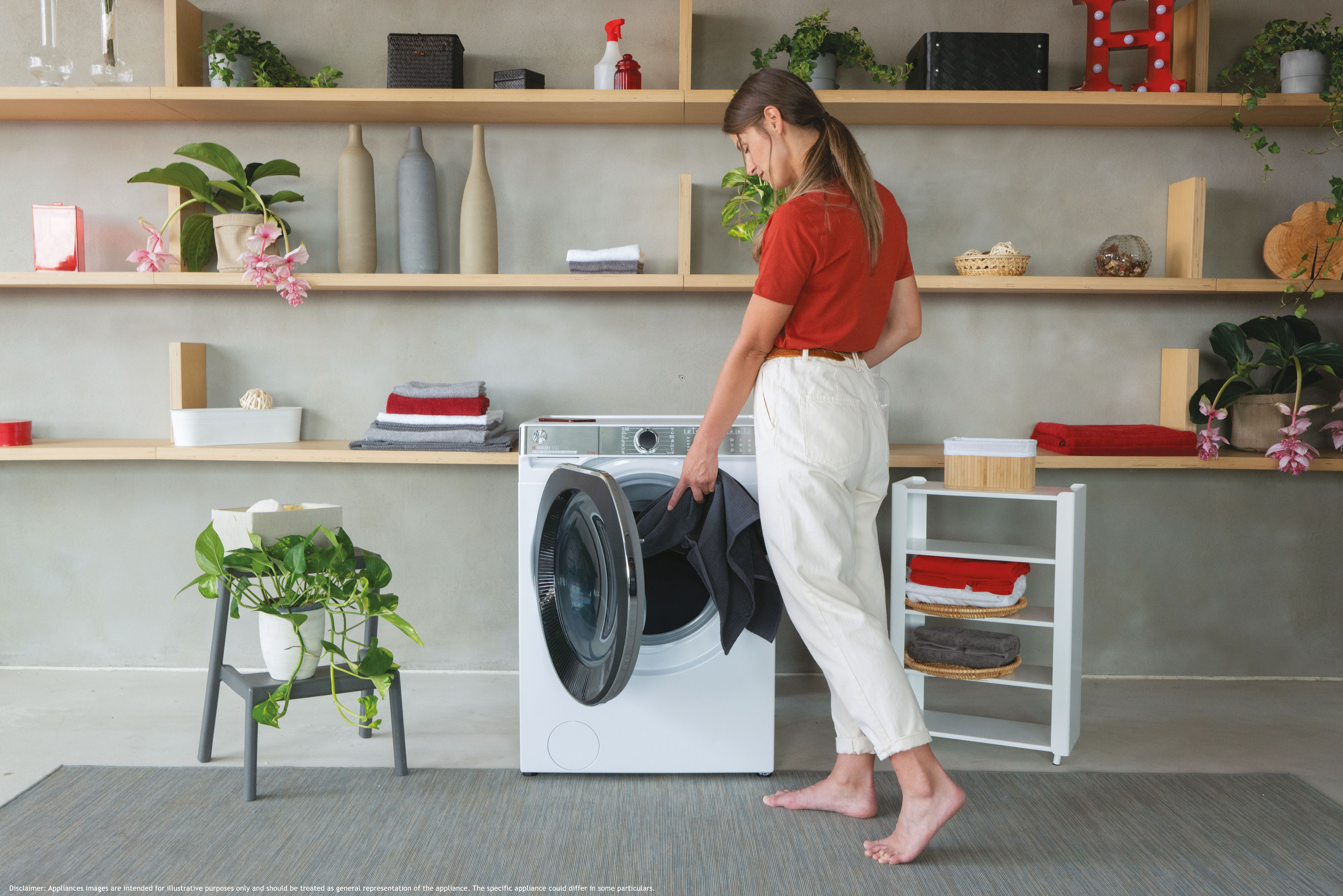Frau in rotem Hemd legt Kleidung in die Waschmaschine. Regale mit Gegenständen an der Wand.