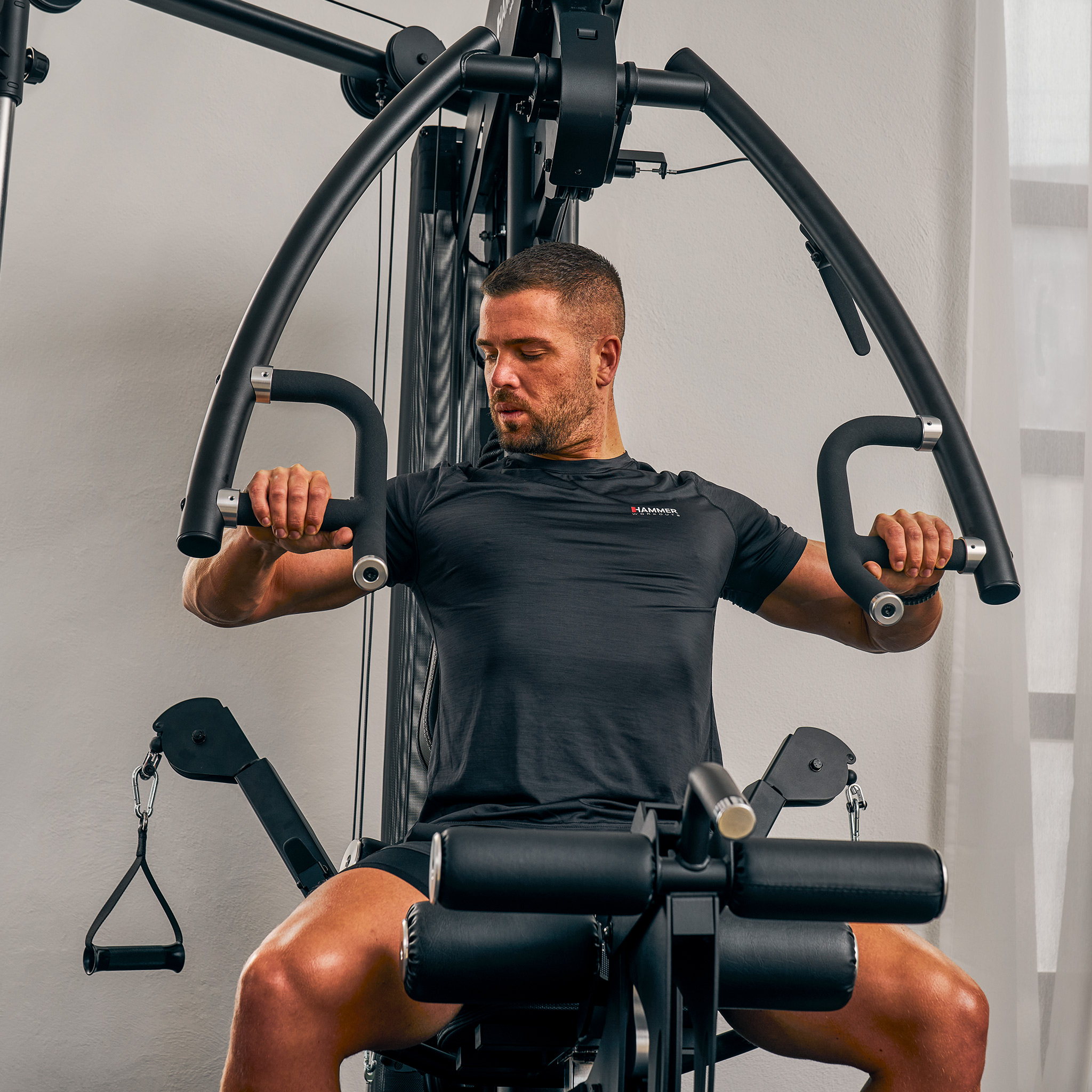 Ein Mann in schwarzer Sportkleidung trainiert an einer Hammer-Fitnessmaschine, Brustpresse.