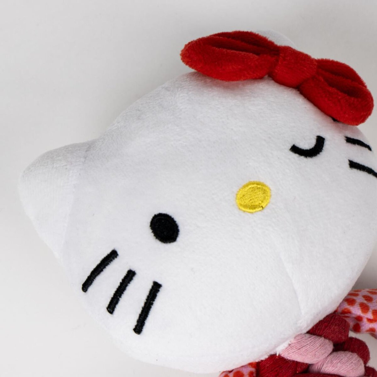 Hello Kitty Plüschkopf mit roter Schleife, schwarzen Augen, Schnurrhaaren und einer gelben Nase. Weißer Hintergrund.