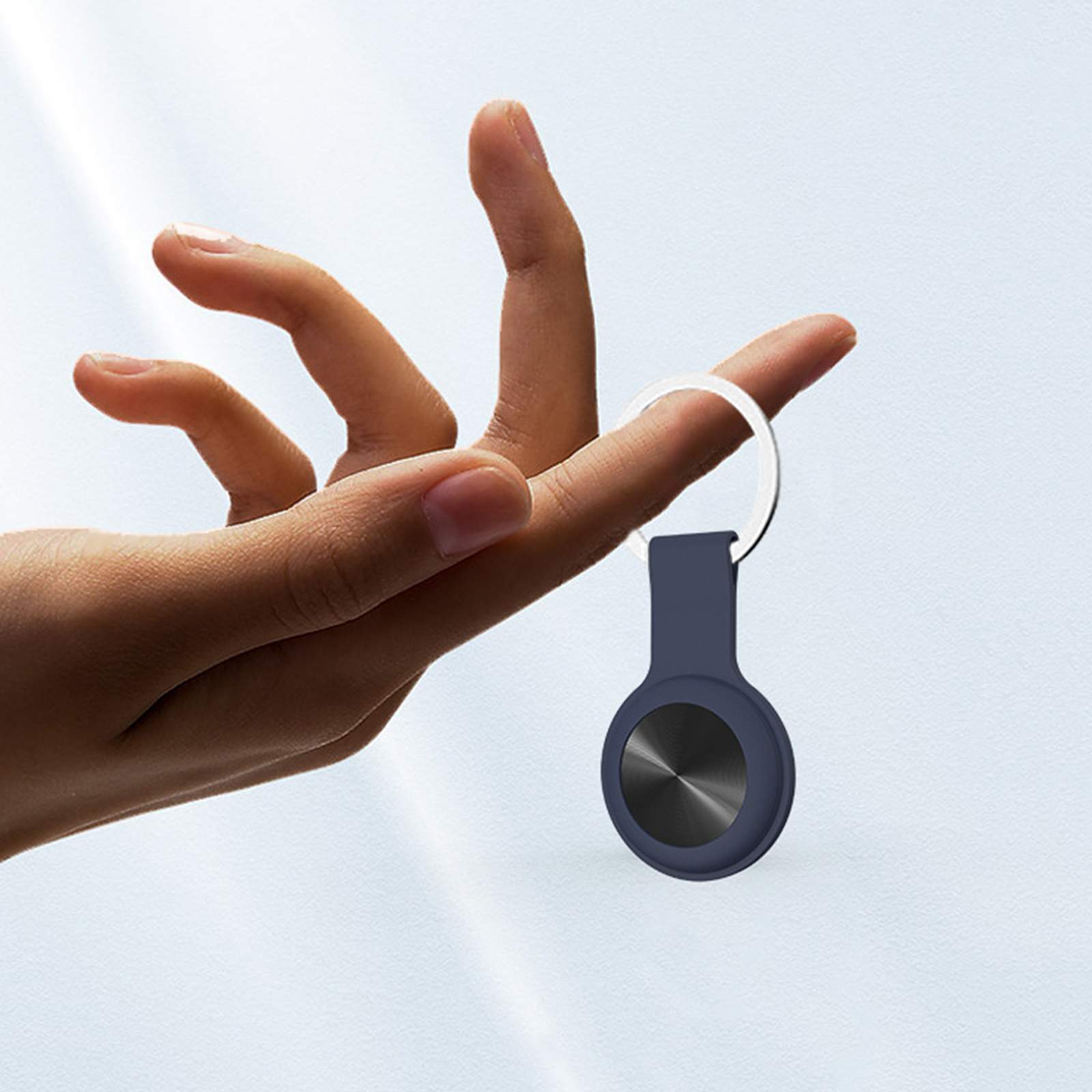 Eine Hand, die ein dunkelblaues AirTag mit silbernem Ring hält.