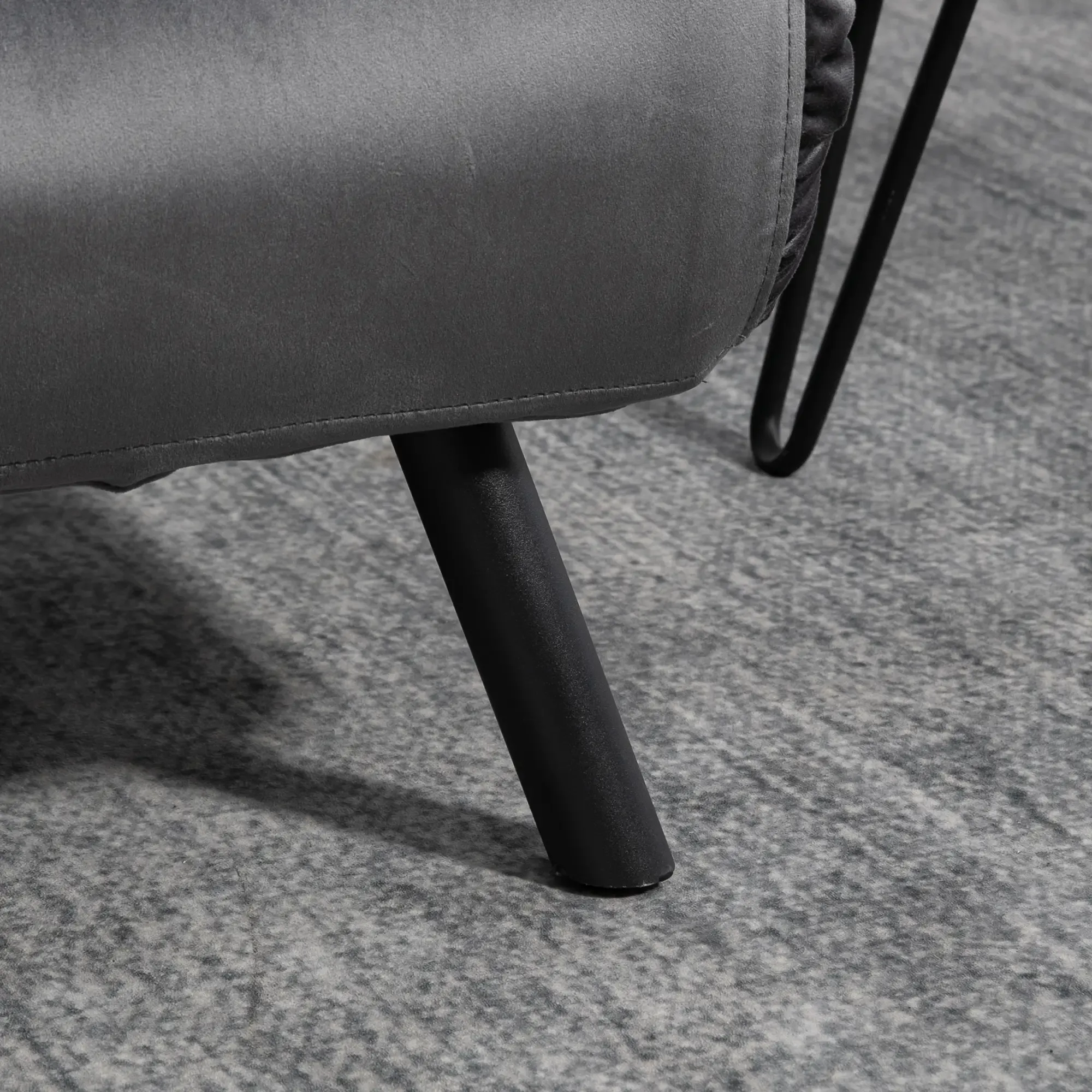 Ein schwarzes Bein eines grauen Sofas ist zu sehen. Das Sofa steht auf einem grauen Teppich.