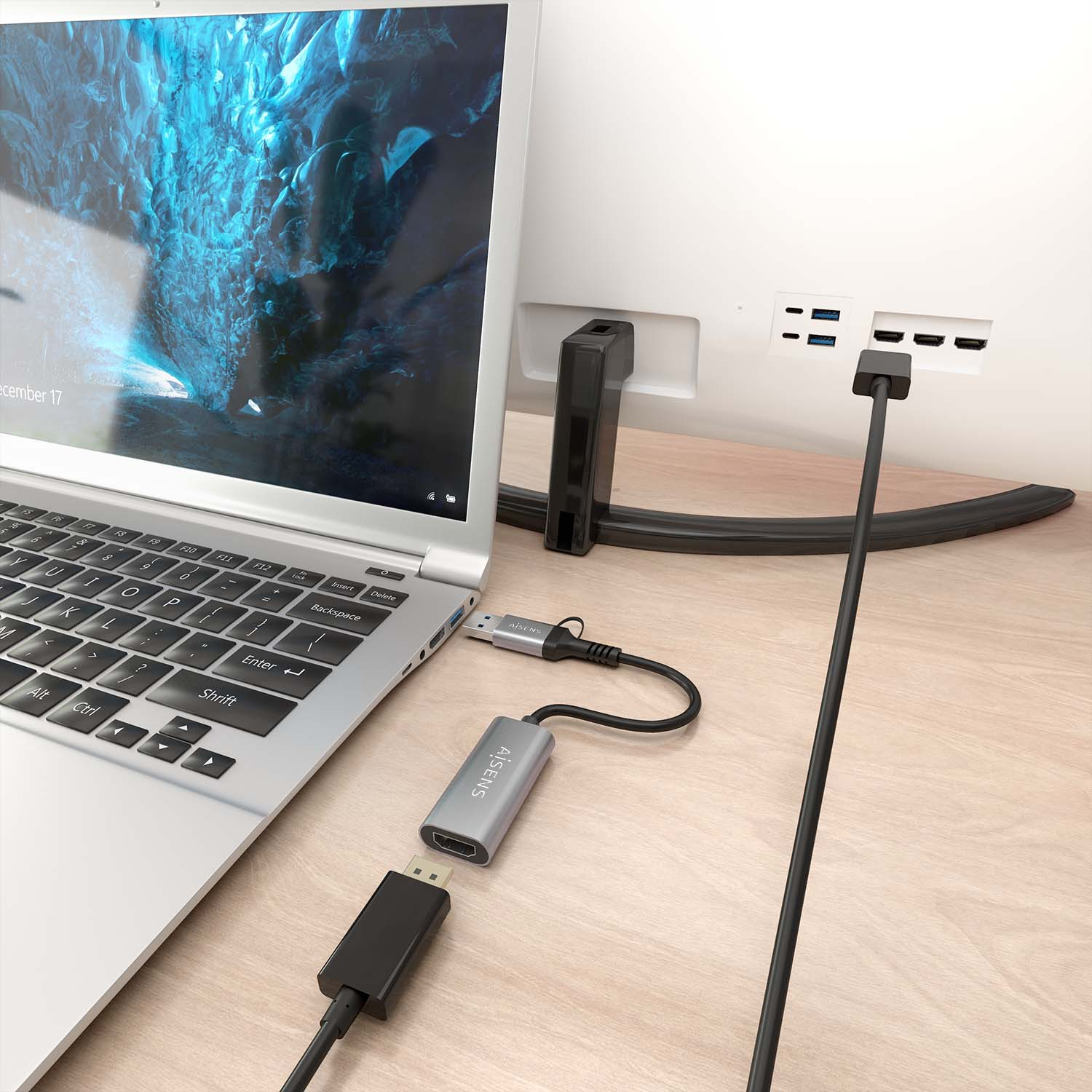 Portátil con adaptador conectado a un monitor y cable negro, sobre superficie de madera.