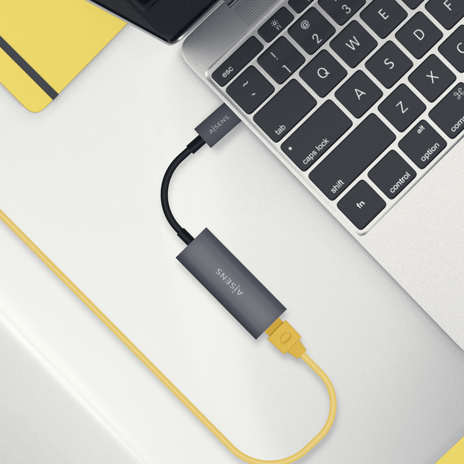 Teclado de portátil con un adaptador Ethernet y cable amarillo.