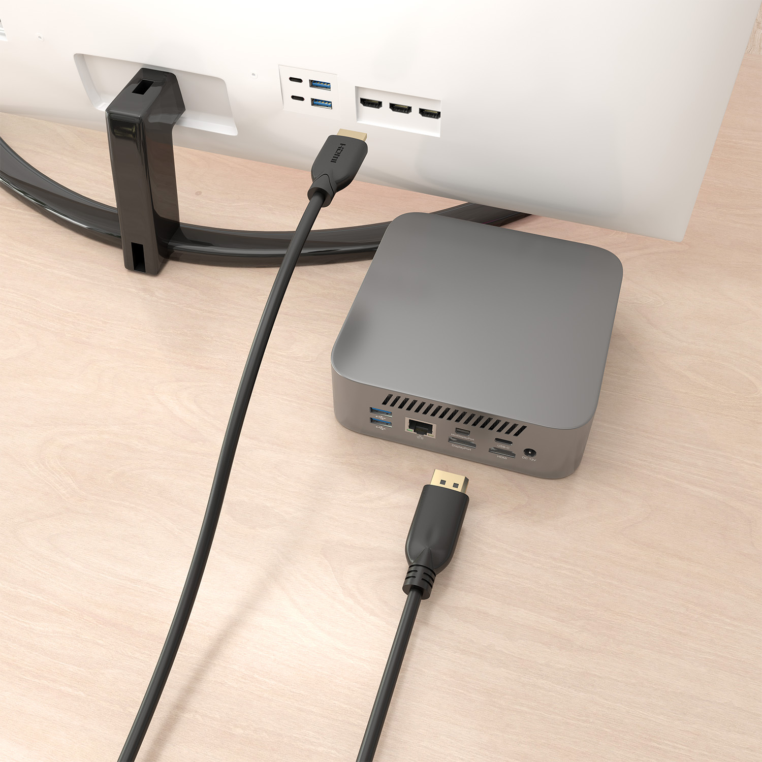 Un cable HDMI conecta una mini PC a un monitor sobre una superficie de madera clara.