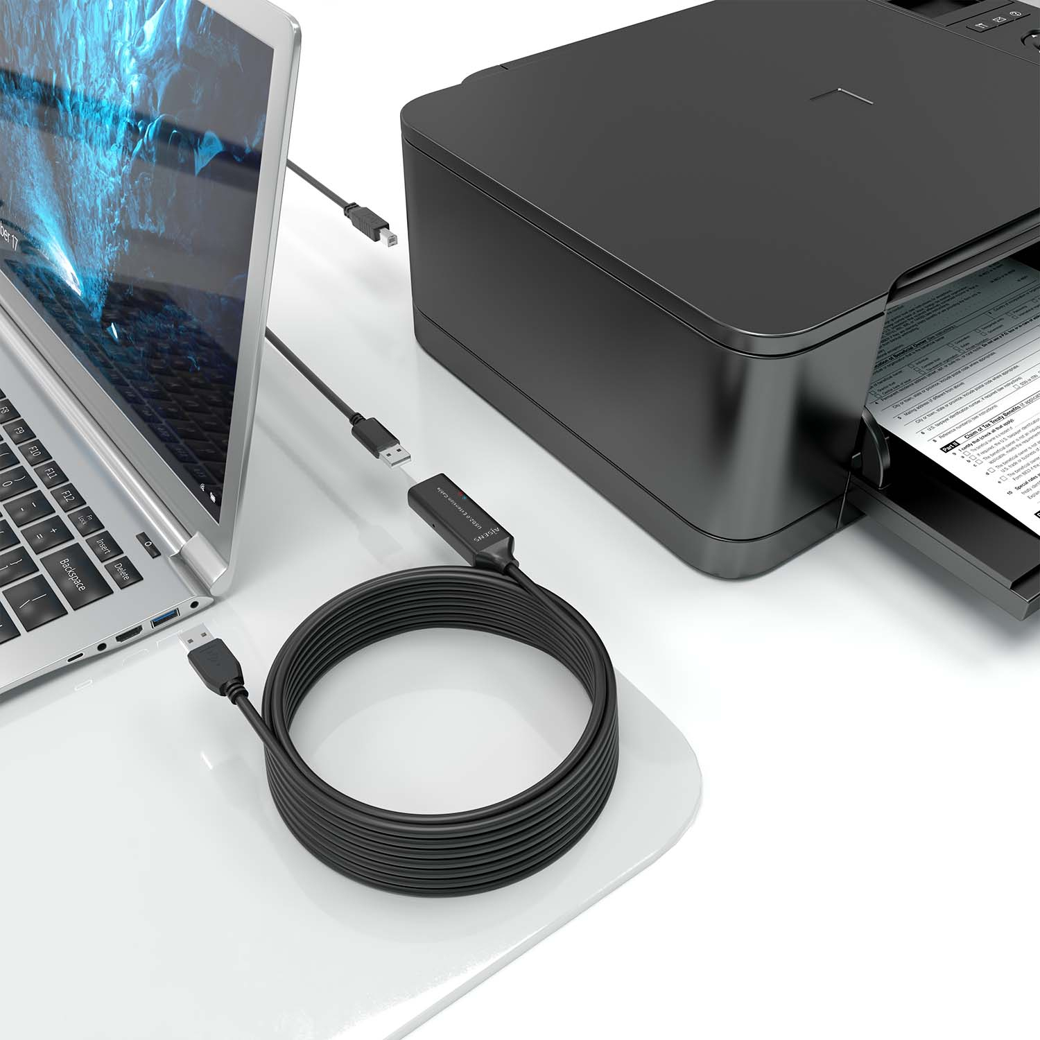 Un portátil, una impresora y un cable de extensión USB están sobre un escritorio blanco contra un fondo blanco.