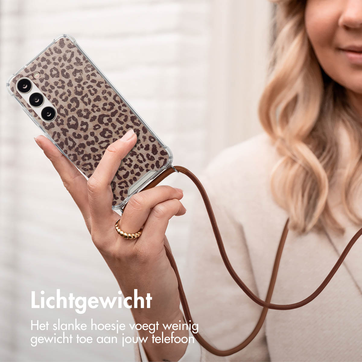Vrouw die een telefoon vasthoudt met een luipaardprint hoesje. De hoes is transparant met een bruin koord.
