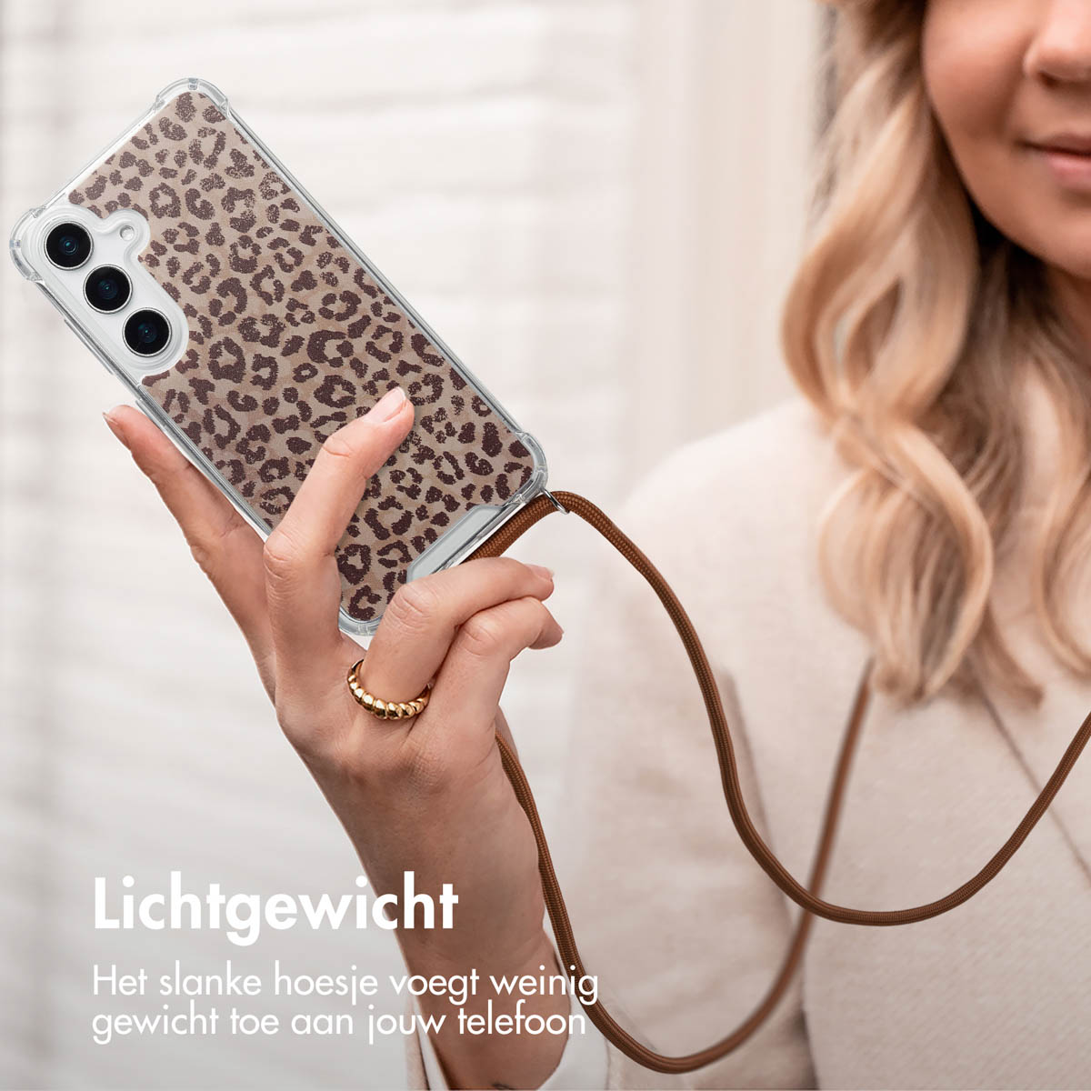 Une femme tient un téléphone avec une coque léopard et une lanière marron.