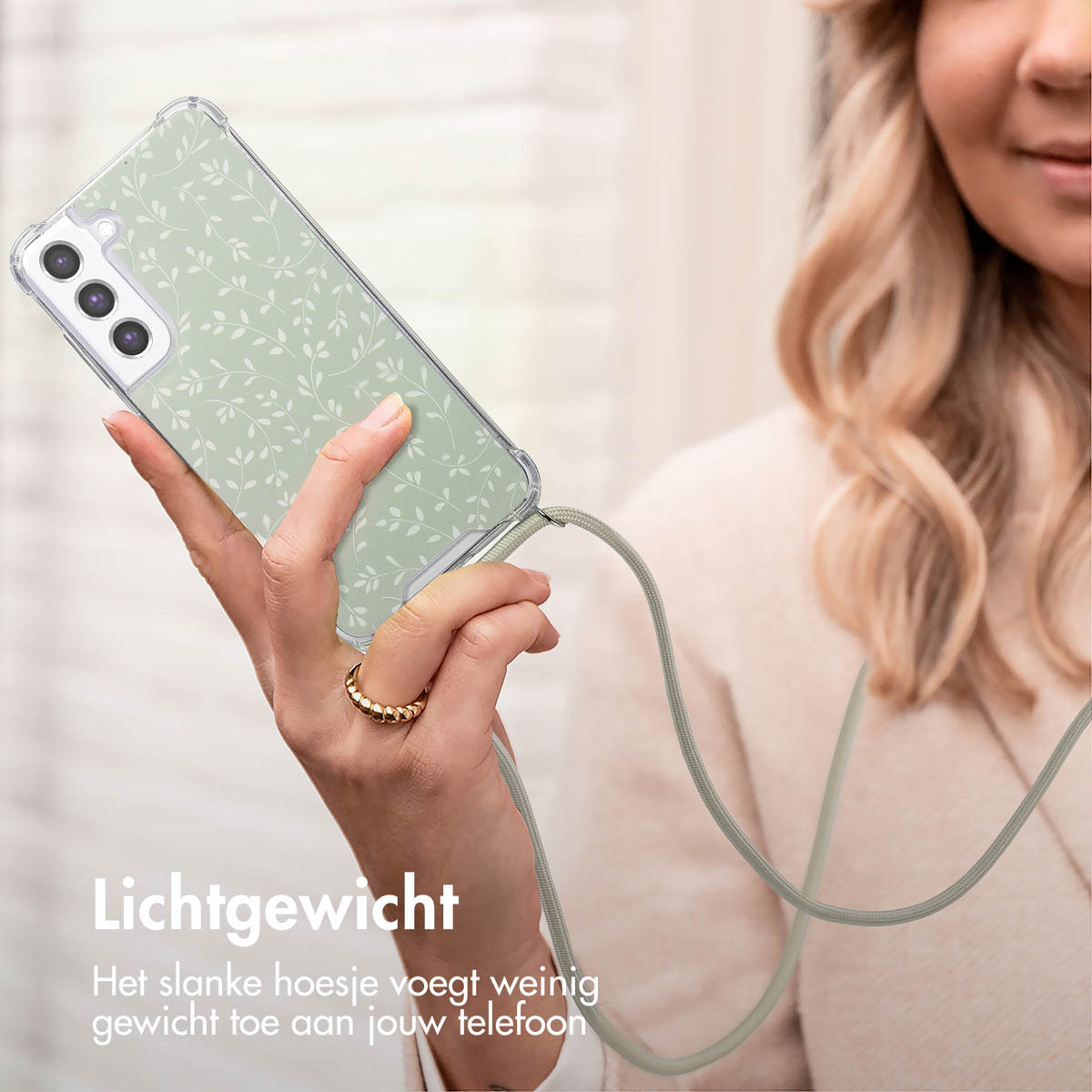 Een vrouw houdt een telefoon vast met een groen bladprint hoesje en een grijze band.