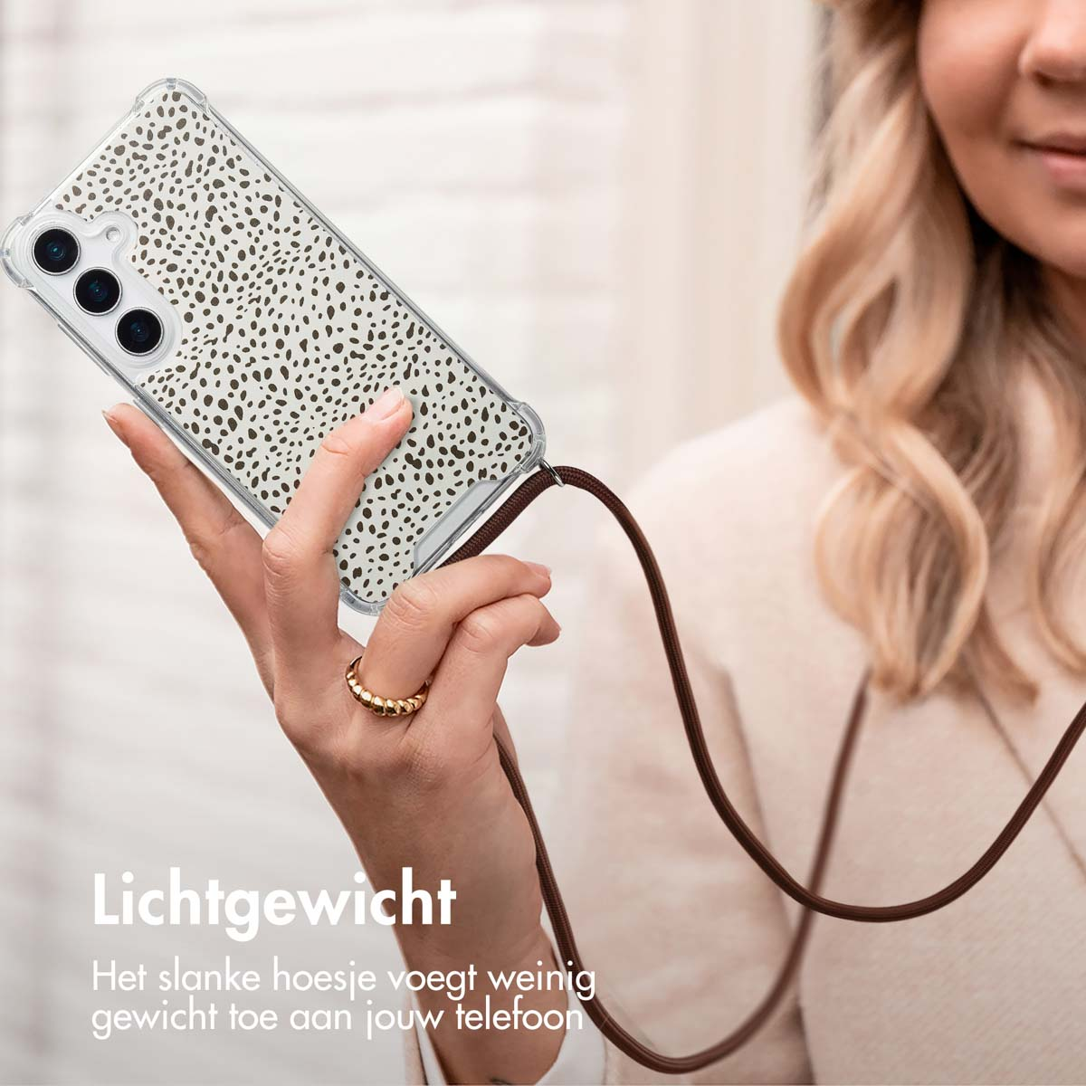 Een vrouw die een telefoon vasthoudt in een doorzichtige hoes met een bruine riem. De hoes heeft een patroon op de achterkant.