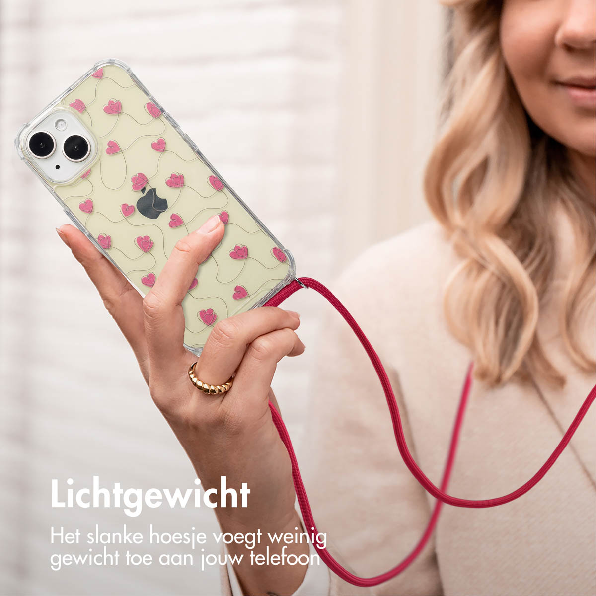 Een vrouw houdt een telefoon vast met een hoesje met hartjespatroon. Er is een rood koord bevestigd. De achtergrond is vaag.