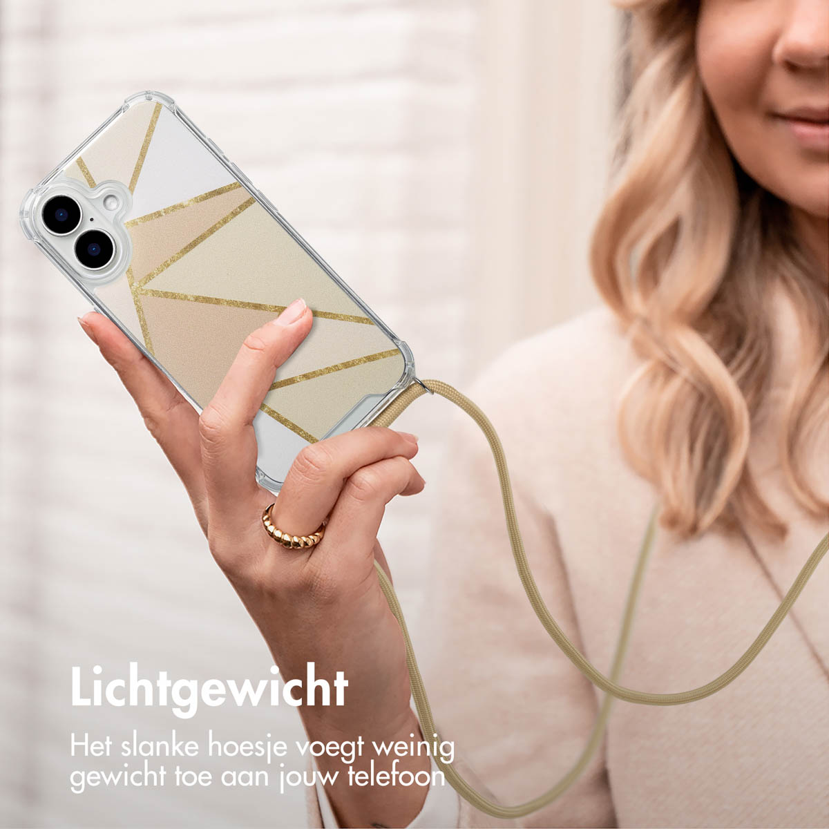 Vrouw houdt telefoon met geometrische hoes, kaki koord. Blond haar, gouden ring. Beige achtergrond.