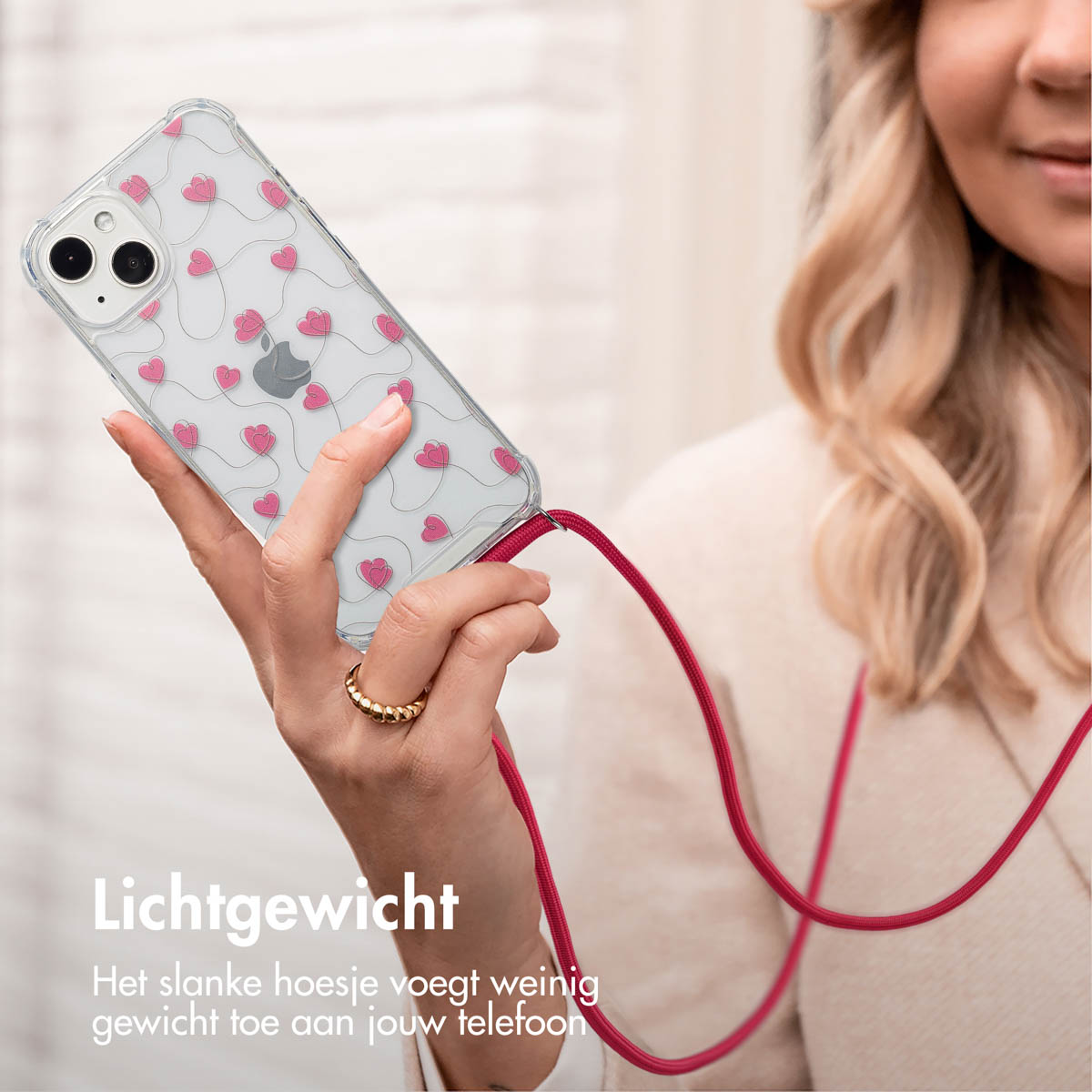 Vrouw houdt telefoon vast met een roze hartjes patroon hoesje en rode lanyard. Tekst: Lichtgewicht. De slanke hoes voegt weinig gewicht toe.