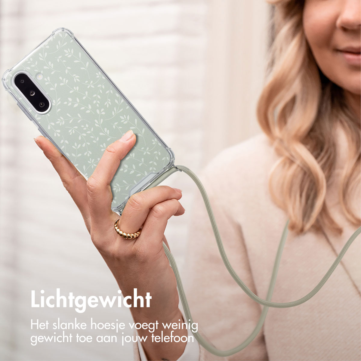 Woman holding a phone with a green floral case. She is wearing a ring. The background is blurry.