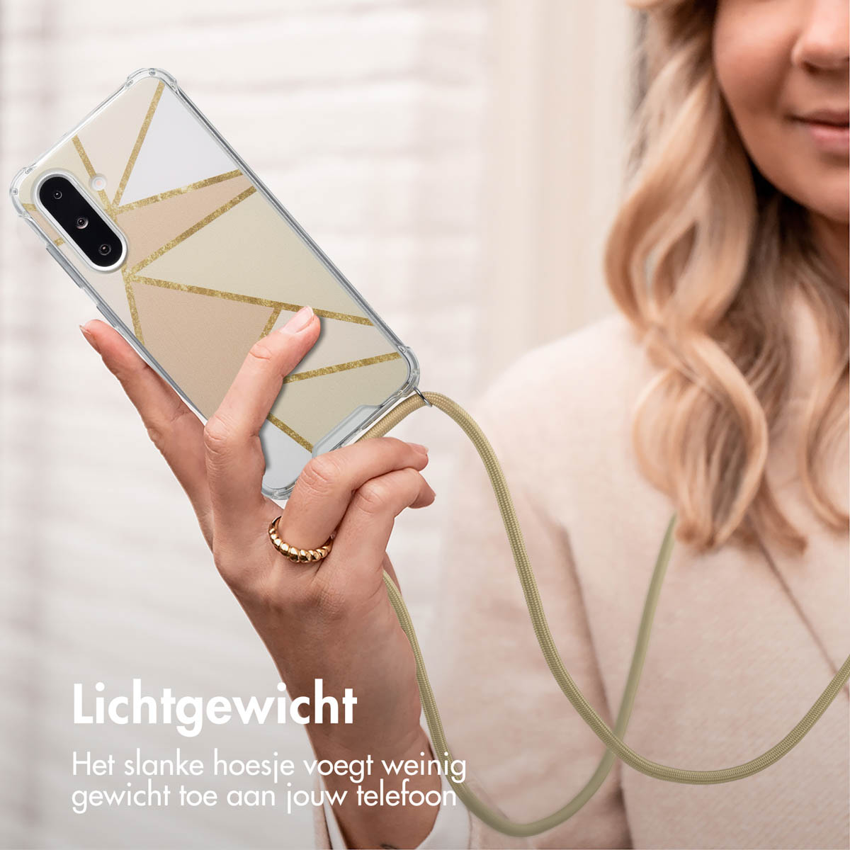 Vrouw die een telefoon vasthoudt met een geometrisch designhoesje, een gouden ring en een telefoonriem.