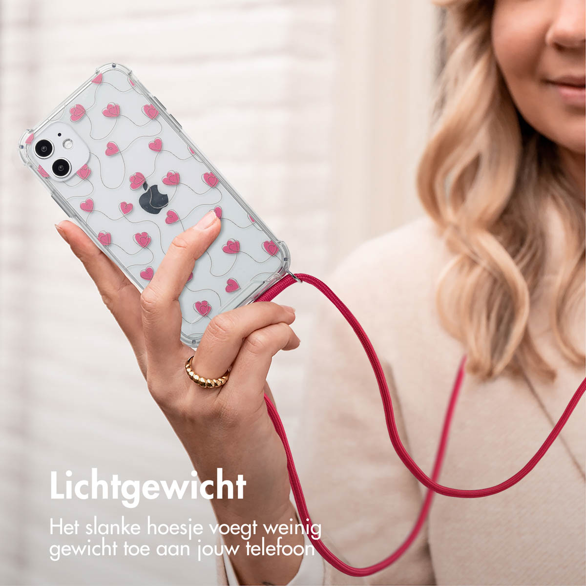 Een vrouw houdt een telefoon vast met een hoesje met hartpatroon. Het hoesje heeft een rode band.