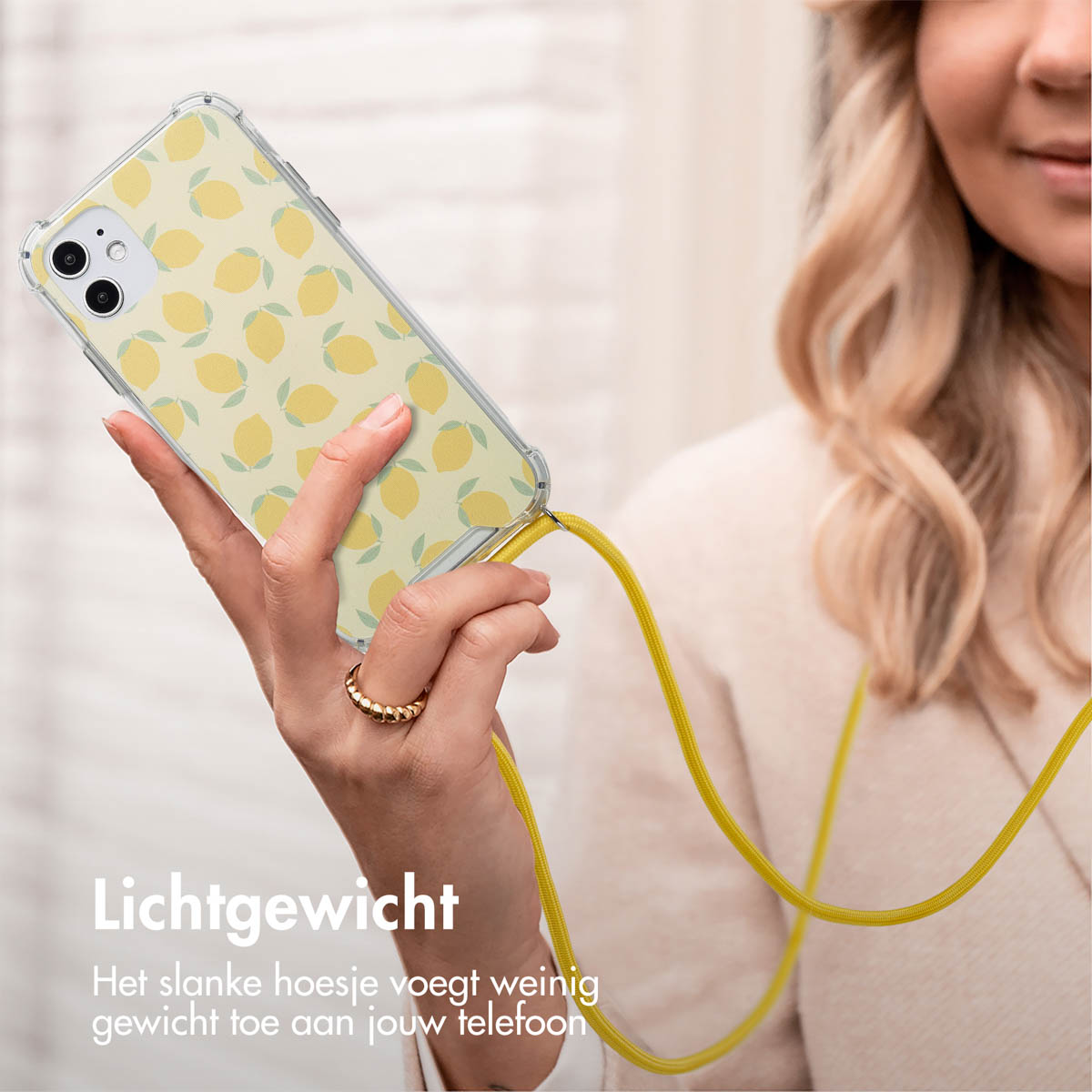 Femme tenant un téléphone avec une coque à motifs de citrons jaunes et un cordon jaune. Texte : 'Léger'. L'arrière-plan est flou.