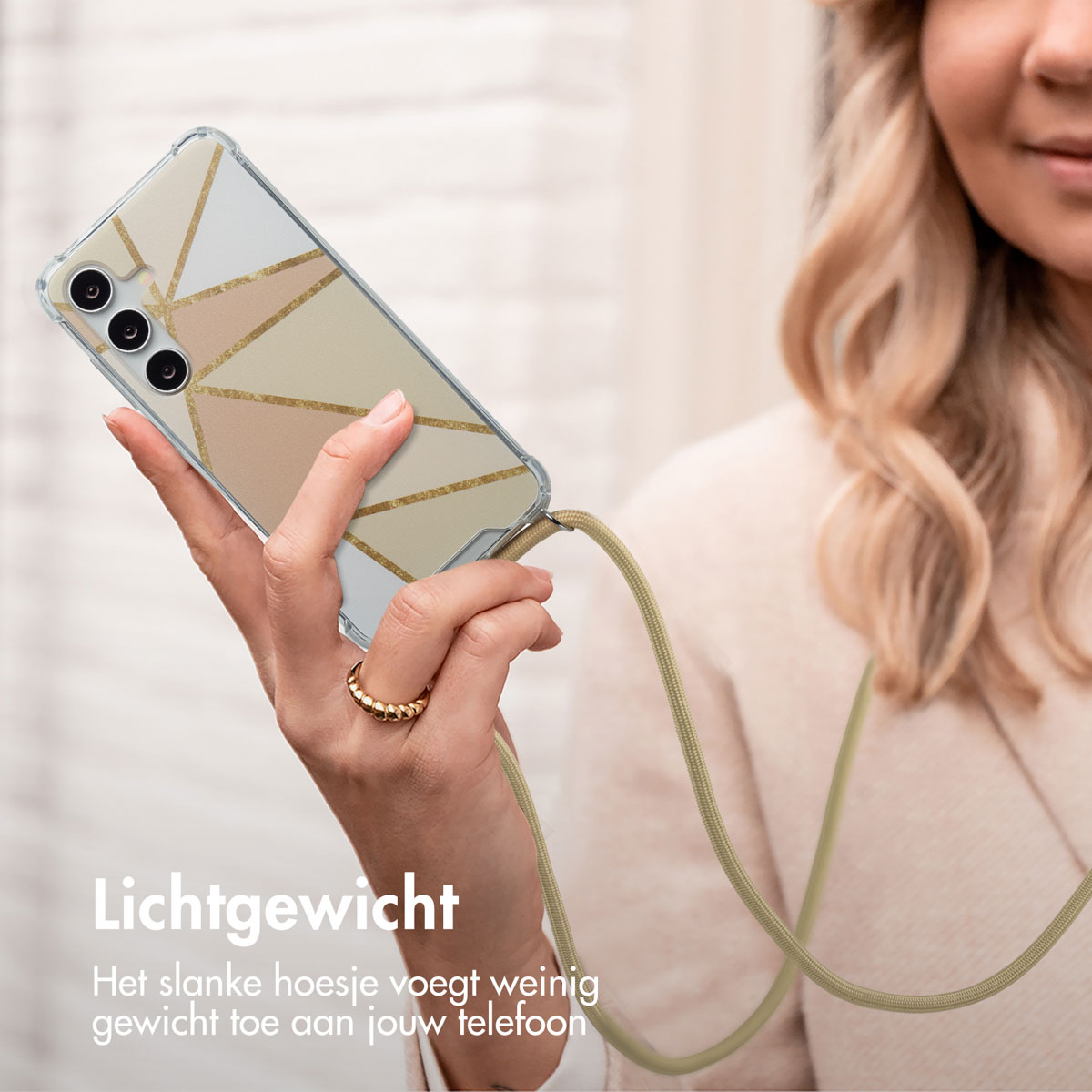 Femme tenant téléphone avec étui géométrique, cordon kaki. Cheveux blonds, bague dorée. Fond beige.