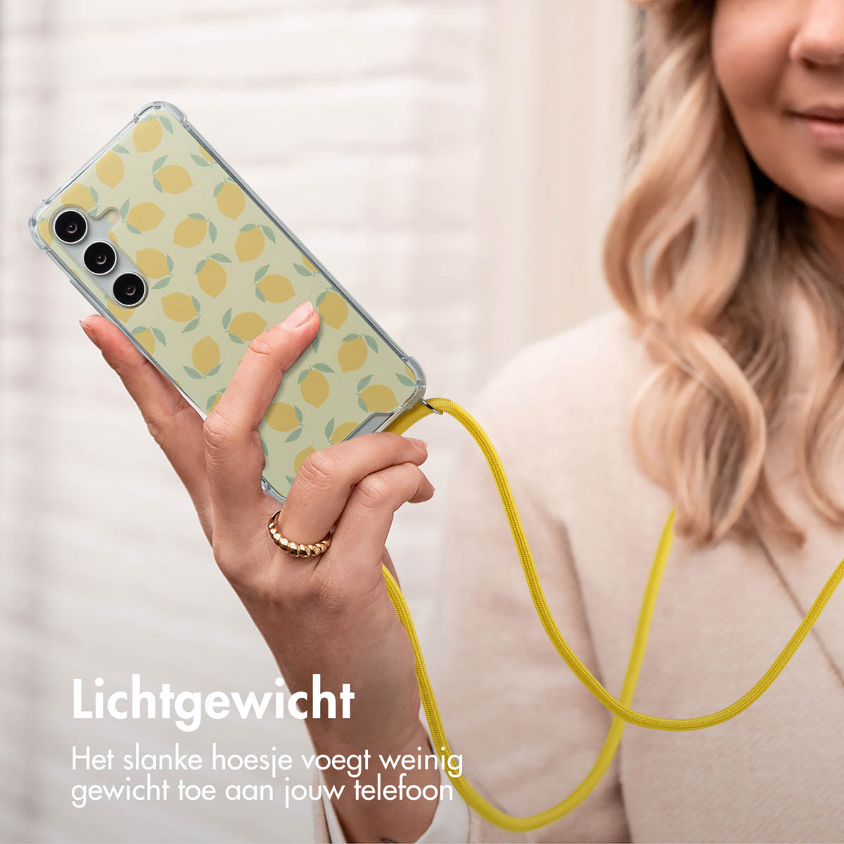 Een vrouw houdt een telefoon vast in een hoesje met citroenpatroon met een gele band. Een gouden ring aan haar vinger.