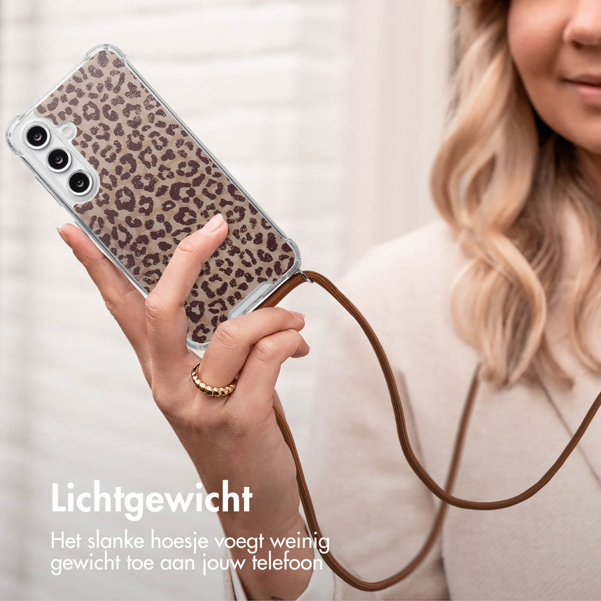 La main d'une femme tenant un téléphone avec une coque imprimée léopard et un cordon. Une bague en or est visible.