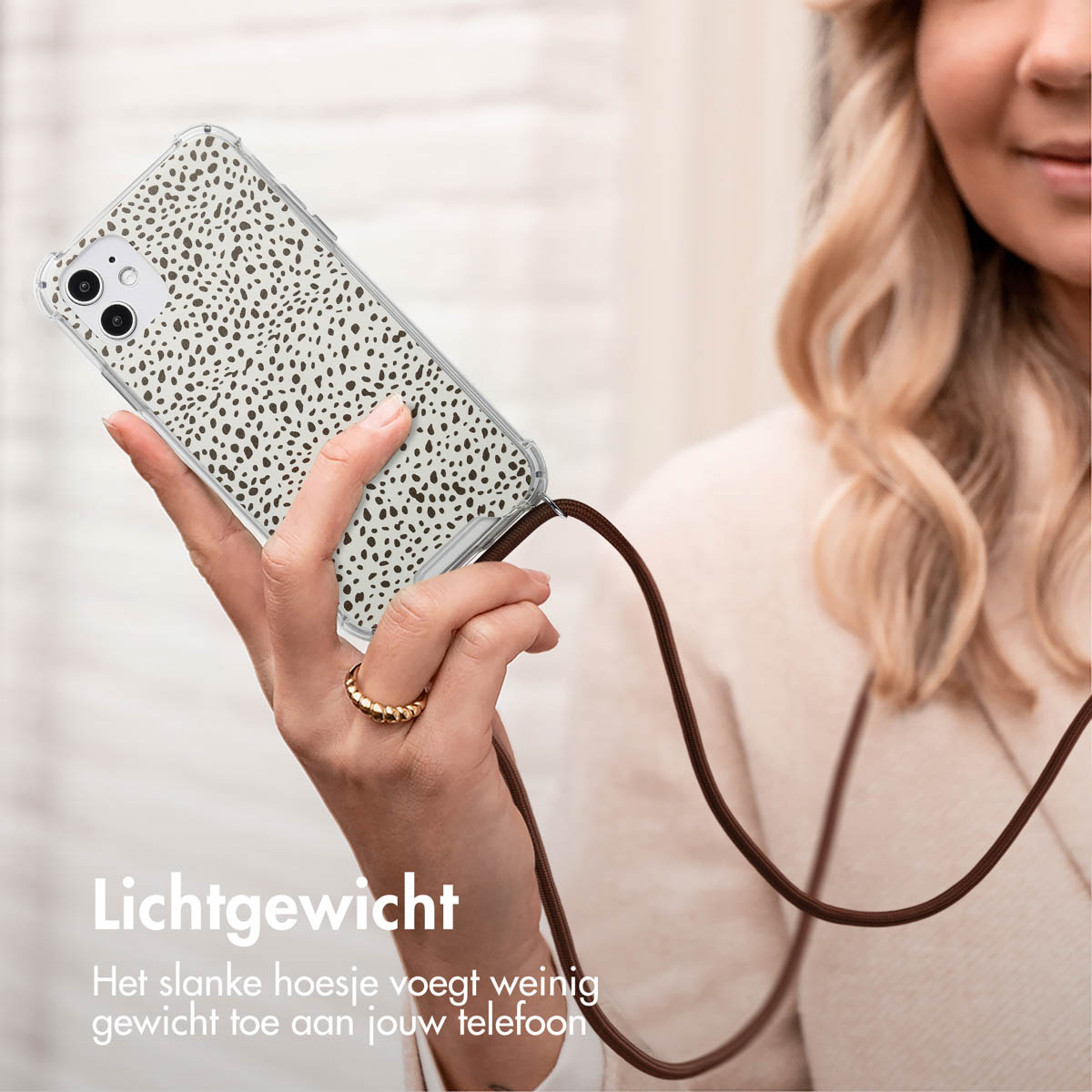 Une femme tient une coque de téléphone avec un motif à pois dalmatien. Le téléphone est suspendu à une lanière marron.
