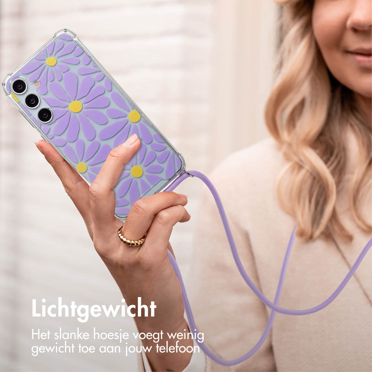 Une femme tient une coque de téléphone avec des fleurs de marguerite. Le téléphone est suspendu à une lanière lavande.