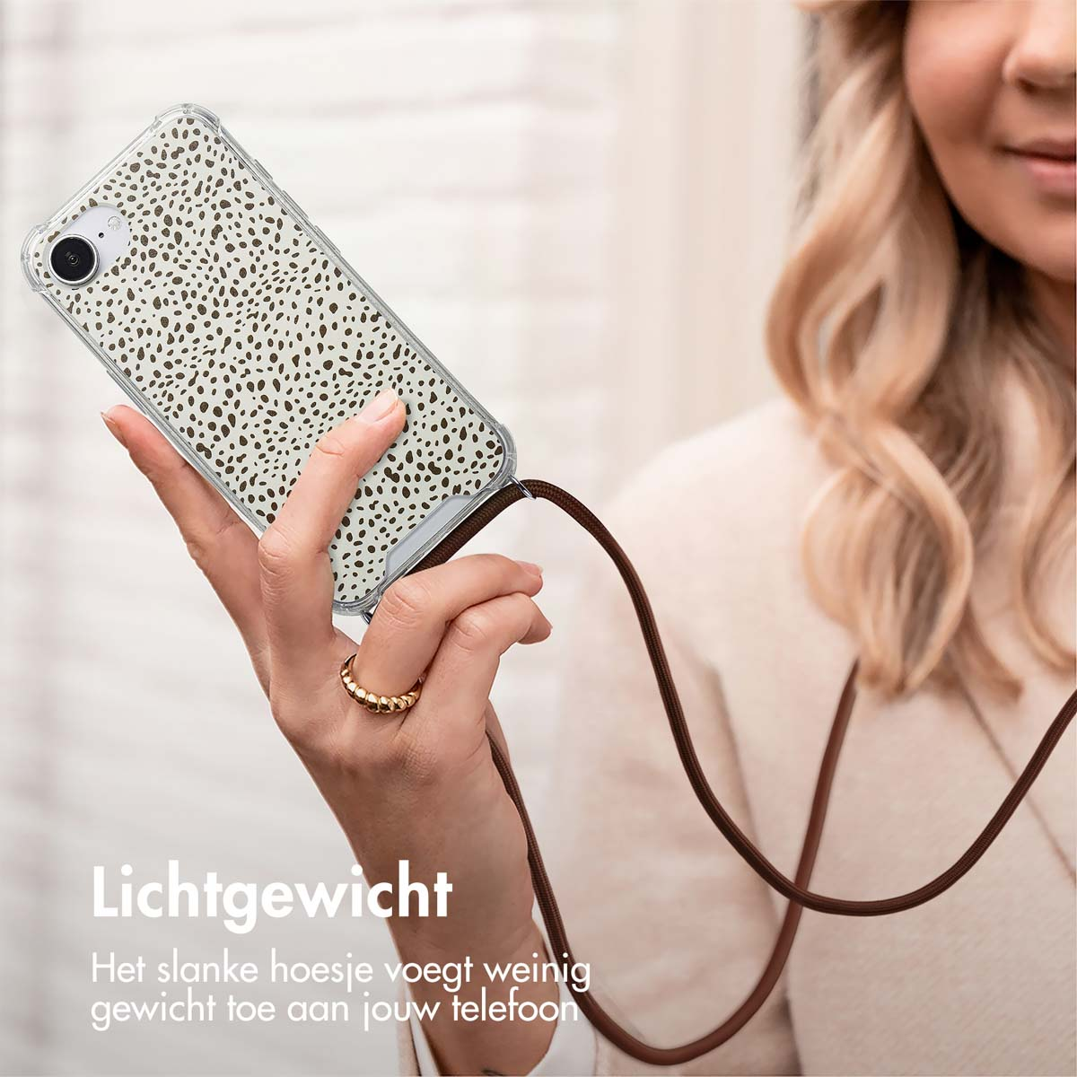 Femme tenant un téléphone avec un motif tacheté marron. Le téléphone a un cordon marron. Une bague dorée à son doigt.