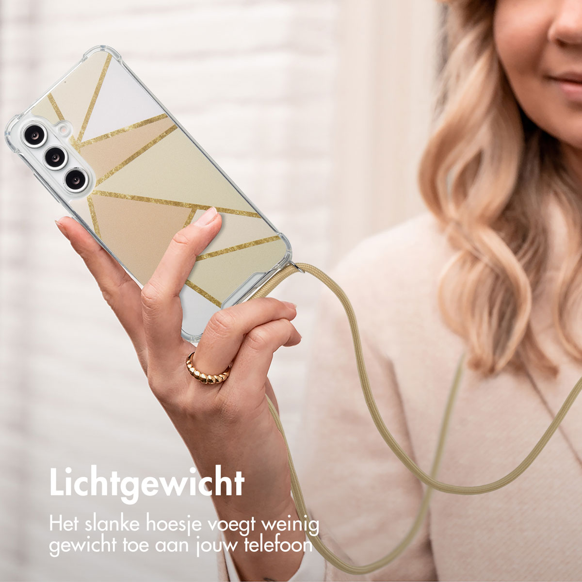 Femme tenant un téléphone avec une sangle. La coque a un motif géométrique doré.
