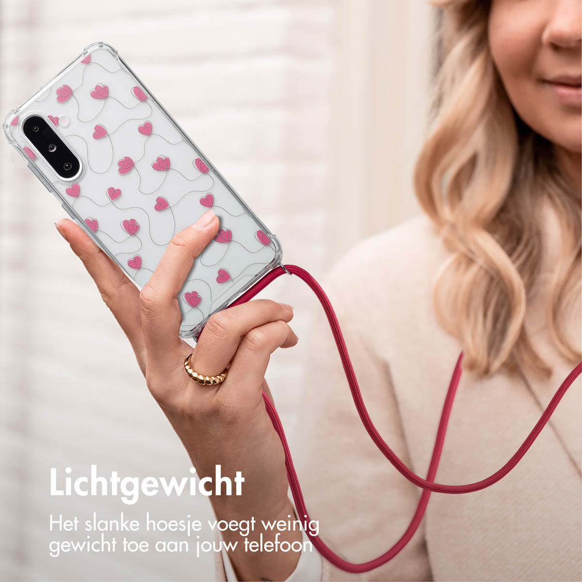 Femme tenant un téléphone avec une sangle. La coque du téléphone a un motif de cœur.