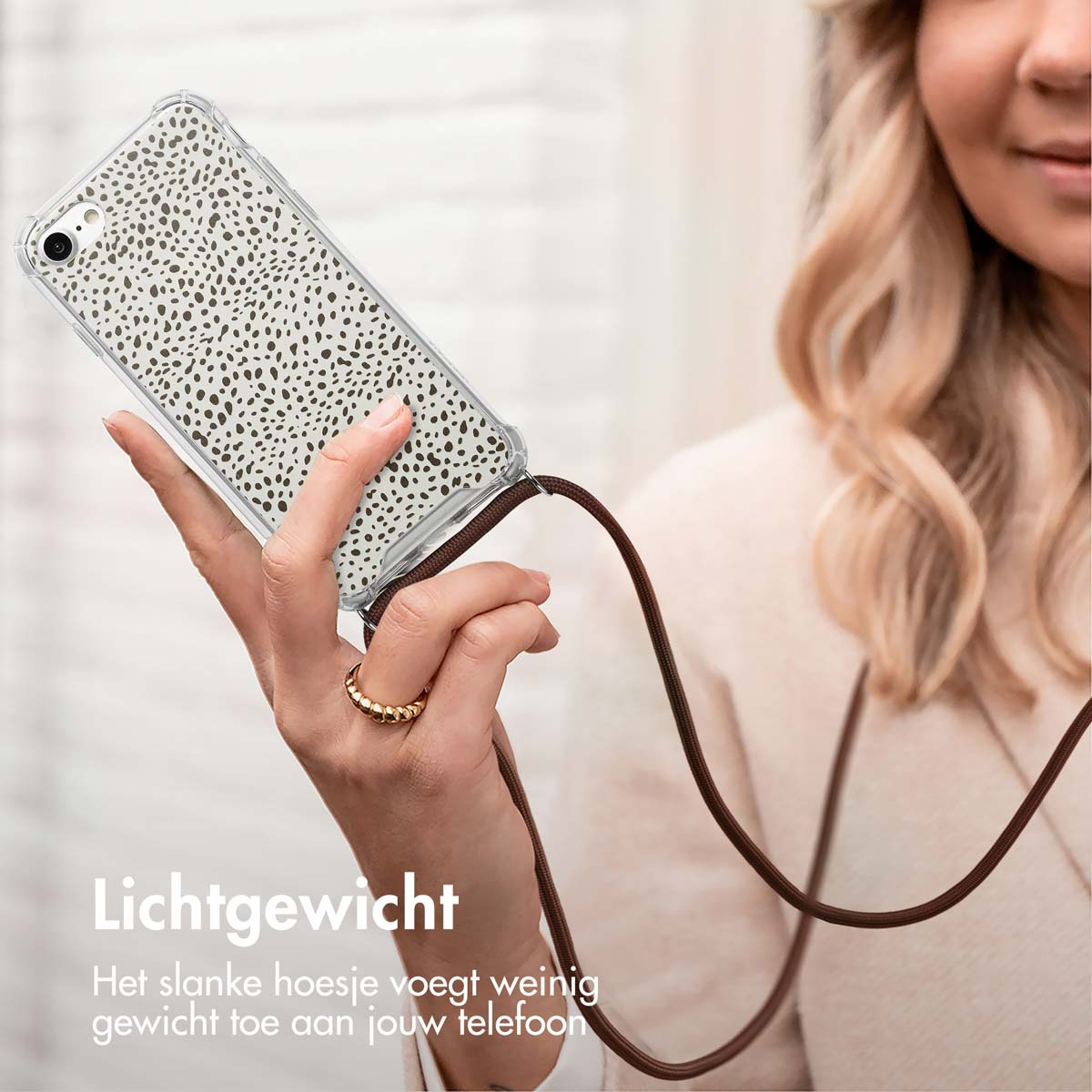 Vrouw houdt telefoon met band vast. Telefoonhoesje heeft witte stippen. Tekst: Lichtgewicht, de slanke hoes voegt weinig gewicht toe.