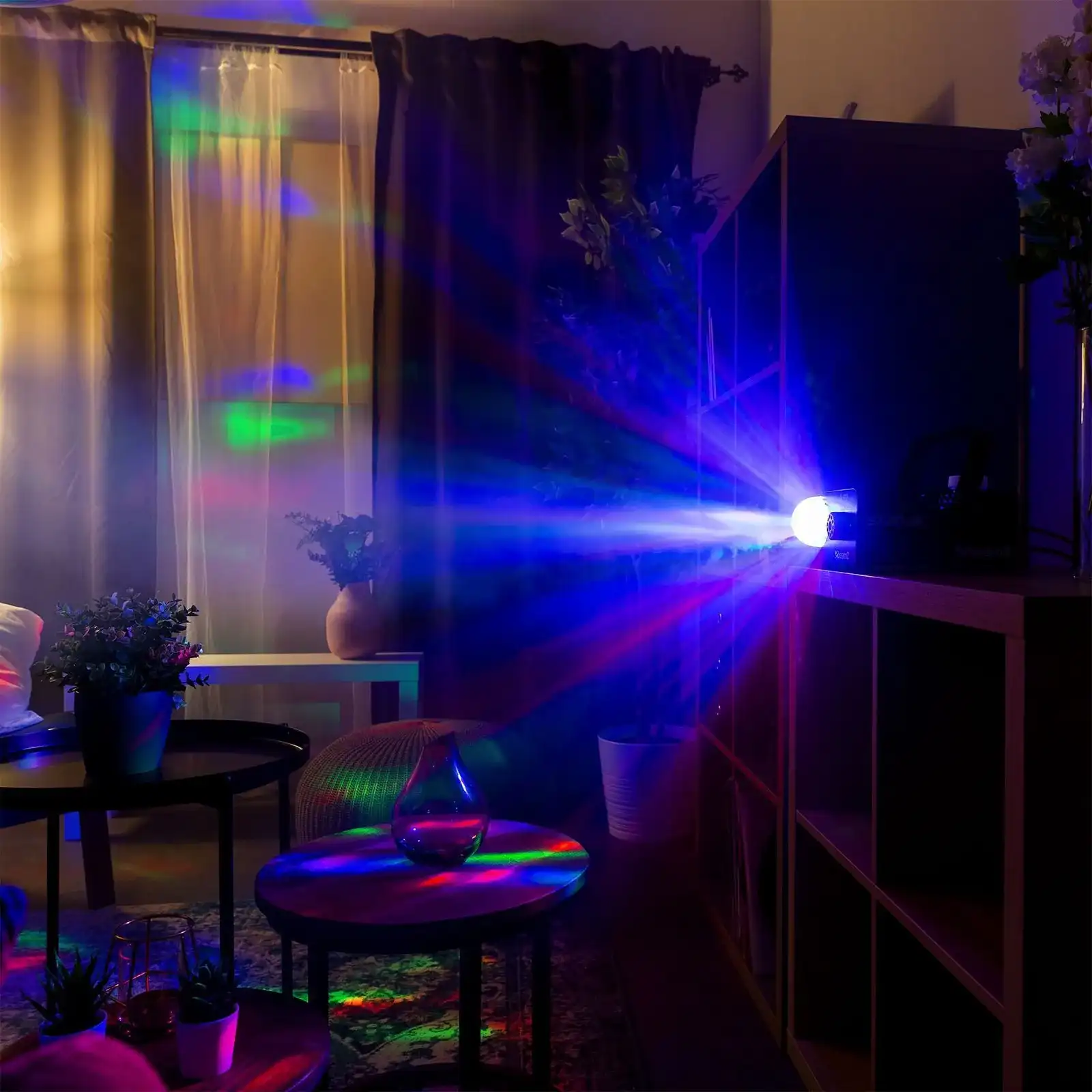 Una habitación oscura con un proyector emitiendo rayos de luz coloridos. Muebles son visibles en primer y segundo plano.