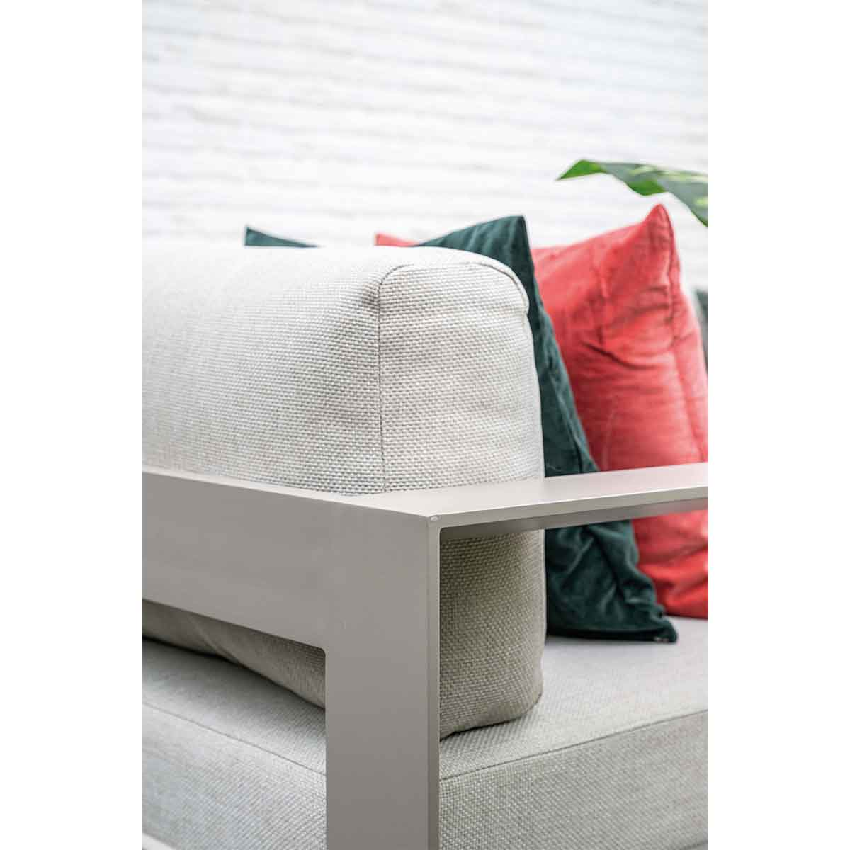 Close-up of a sofa armrest with green and red pillows on a white brick wall.