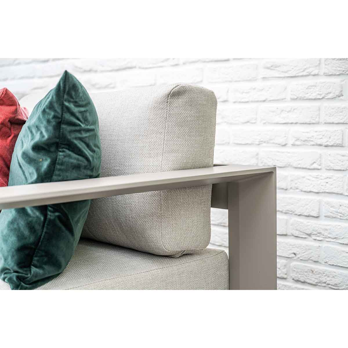Close up of a sofa armrest with a green and red pillow on a white brick wall.